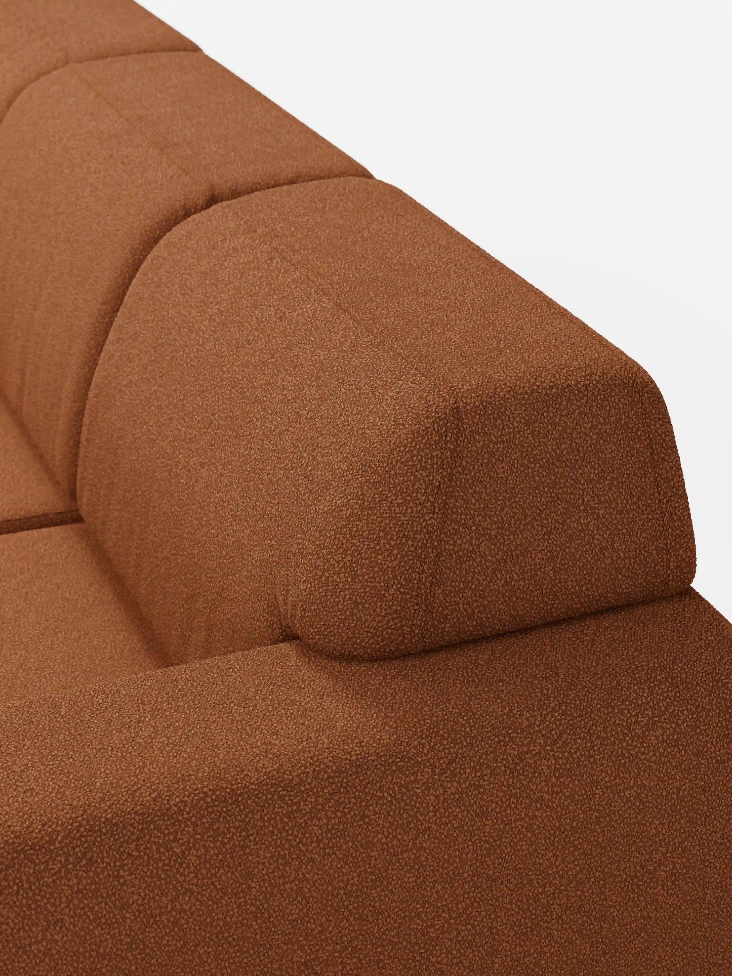 Primo piano del divano Orbit con 3 sedute scorrevoli e allungabili di divitt.sbs, caratterizzato da un rivestimento color ruggine con texture, realizzato in tessuto smacchiabile T33 effetto cotone. L’immagine mette in risalto lo schienale e il cuscino di seduta dalle forme delicatamente arrotondate, attirando l’attenzione sul motivo discreto del tessuto e sulle linee pulite e geometriche del divano, che risaltano sullo sfondo bianco a tinta unita.