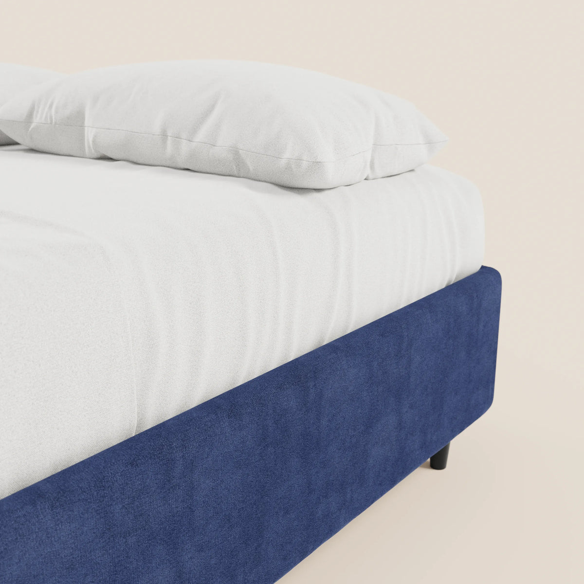 Un primo piano del letto sommier imbottito con contenitore ERON di Letti.store, con un cuscino e un lenzuolo bianchi sul materasso. Il tessuto impermeabile blu scuro, certificato Oeko-Tex, conferisce un tocco di modernità sullo sfondo beige chiaro.