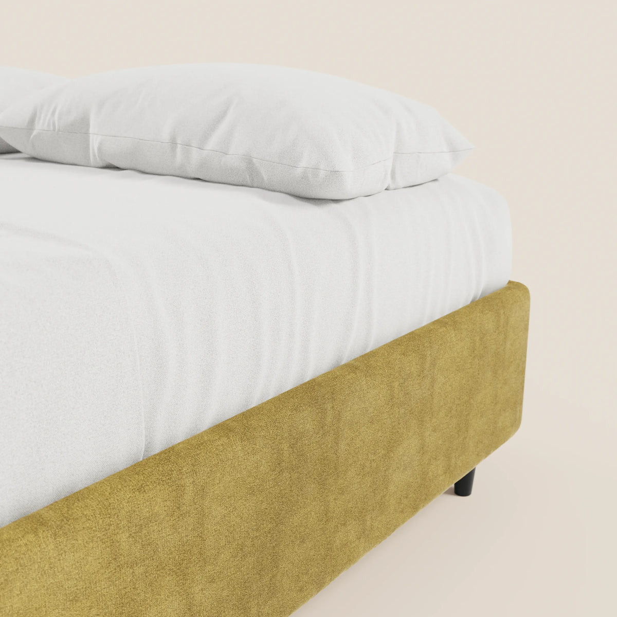 Un primo piano del letto sommier imbottito ERON di Letti.store, caratterizzato da un tessuto impermeabile giallo senape certificato Oeko-Tex e da gambe corte nere, con lenzuolo con angoli e cuscino bianchi, in contrasto con una parete chiara e liscia.