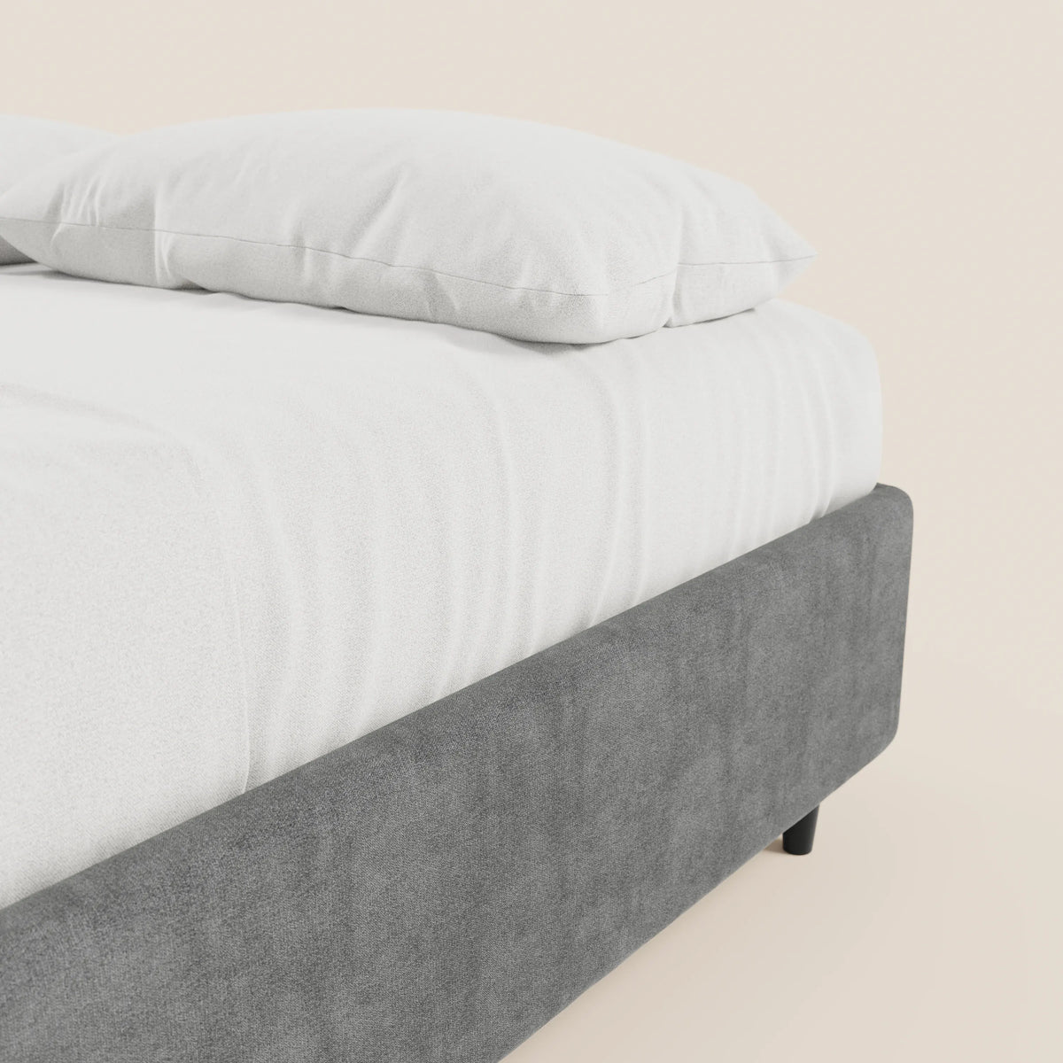 Un primo piano mostra il letto sommier imbottito ERON di Letti.store, realizzato in tessuto impermeabile certificato Oeko-Tex, con lenzuolo con angoli e cuscino bianchi, che fa da contrasto con una parete beige chiaro a tinta unita, creando un look pulito e moderno per la camera da letto.