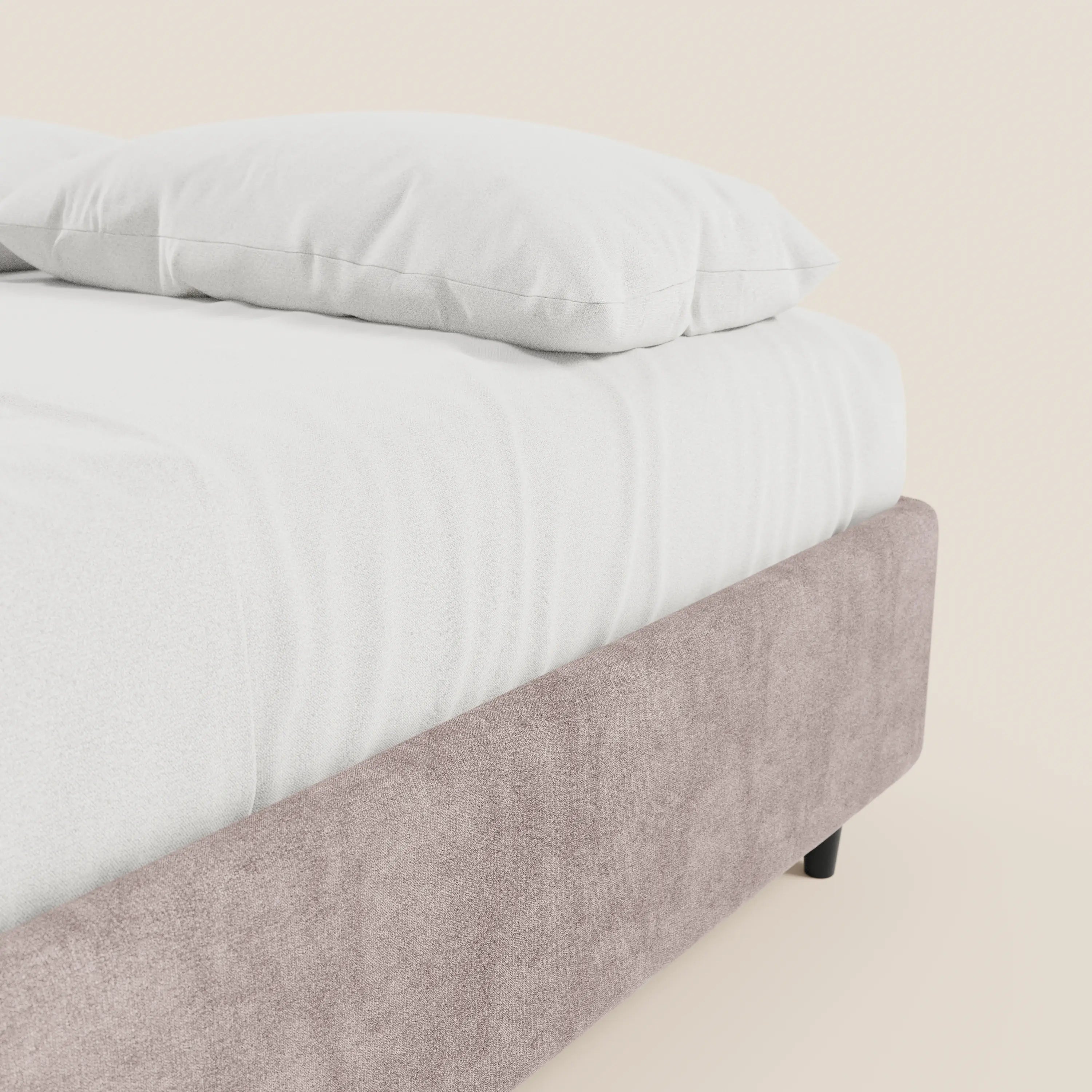 Un primo piano del letto sommier imbottito ERON di Letti.store con lenzuolo e cuscino bianchi. La struttura del letto e la base contenitore, realizzate in tessuto impermeabile color beige chiaro e certificate Oeko-Tex, sono riprese su uno sfondo di parete chiara e liscia, che mette in risalto l’angolo del materasso.