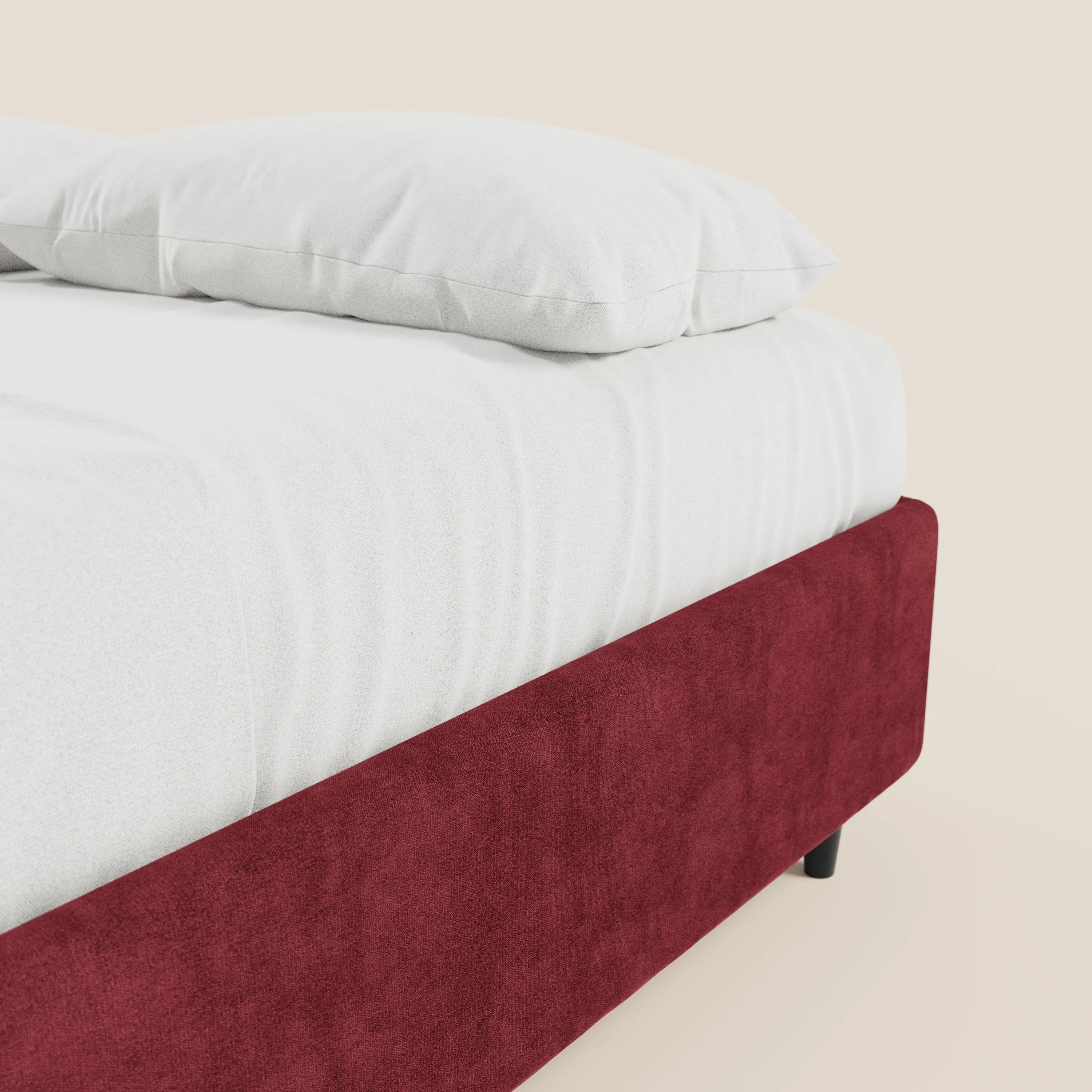 Un primo piano del letto sommier imbottito con contenitore ERON di Letti.store mostra un cuscino bianco e un lenzuolo con angoli adagiati sulla struttura imbottita color bordeaux, impermeabile e certificata Oeko-Tex, che crea un contrasto con lo sfondo chiaro.