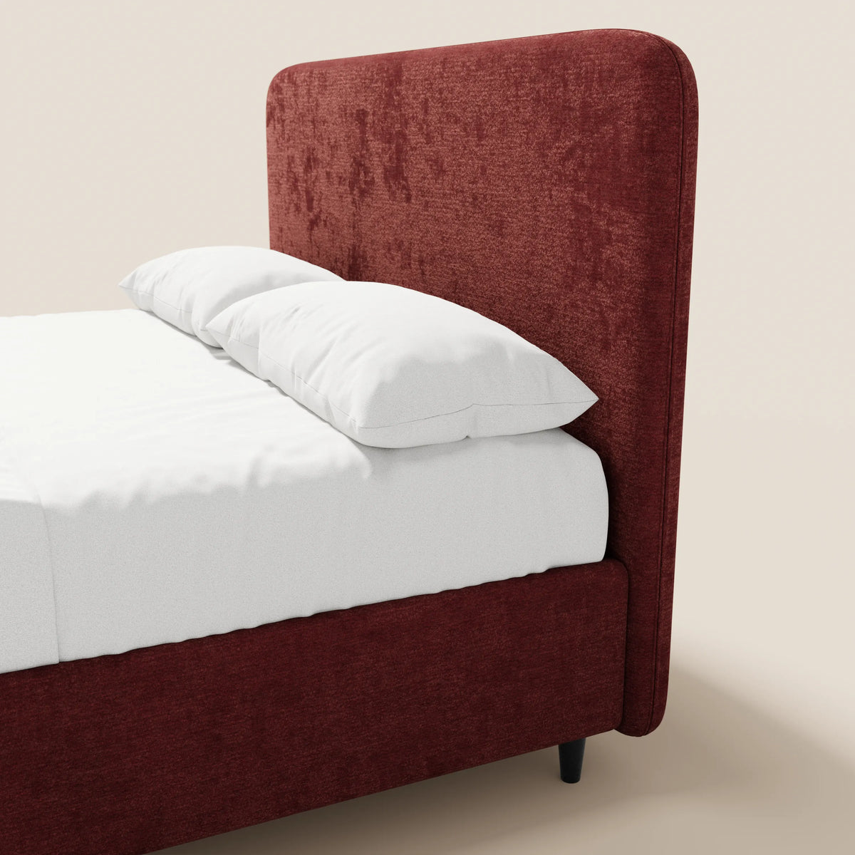 Il letto imbottito KAELOS minimal di Letti.store presenta una testiera alta e arrotondata in ciniglia e una struttura di colore rosso intenso, con piedini alti e vano contenitore. Nell’immagine è raffigurato in parte con lenzuola e cuscini di un bianco candido, su uno sfondo beige chiaro.