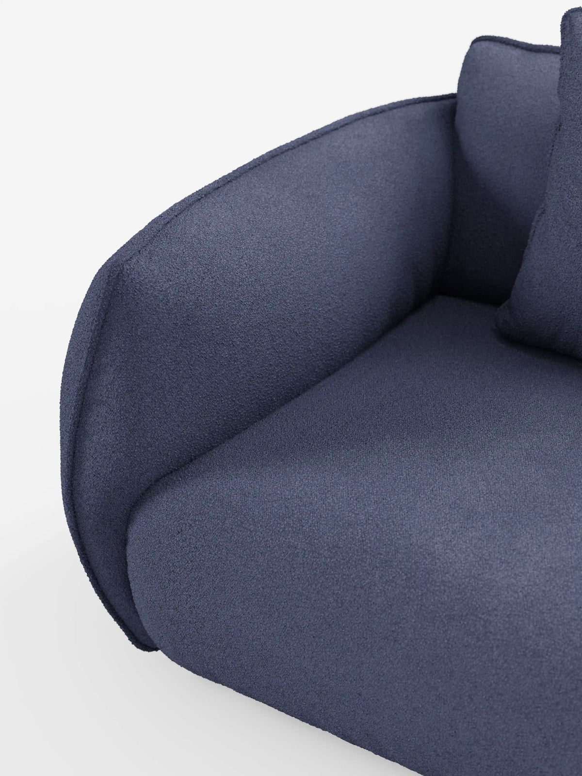 Primo piano del divano angolare con penisola componibile Nimbus di divitt.sbs, rivestito in tessuto T33 blu scuro, con effetto cotone e texture, resistente alle macchie. I braccioli arrotondati e il cuscino di seduta ne sottolineano la morbida imbottitura, mentre un cuscino coordinato è parzialmente visibile nell’angolo in alto a destra su uno sfondo bianco a tinta unita, mettendo in risalto il design moderno di questo divano contemporaneo.
