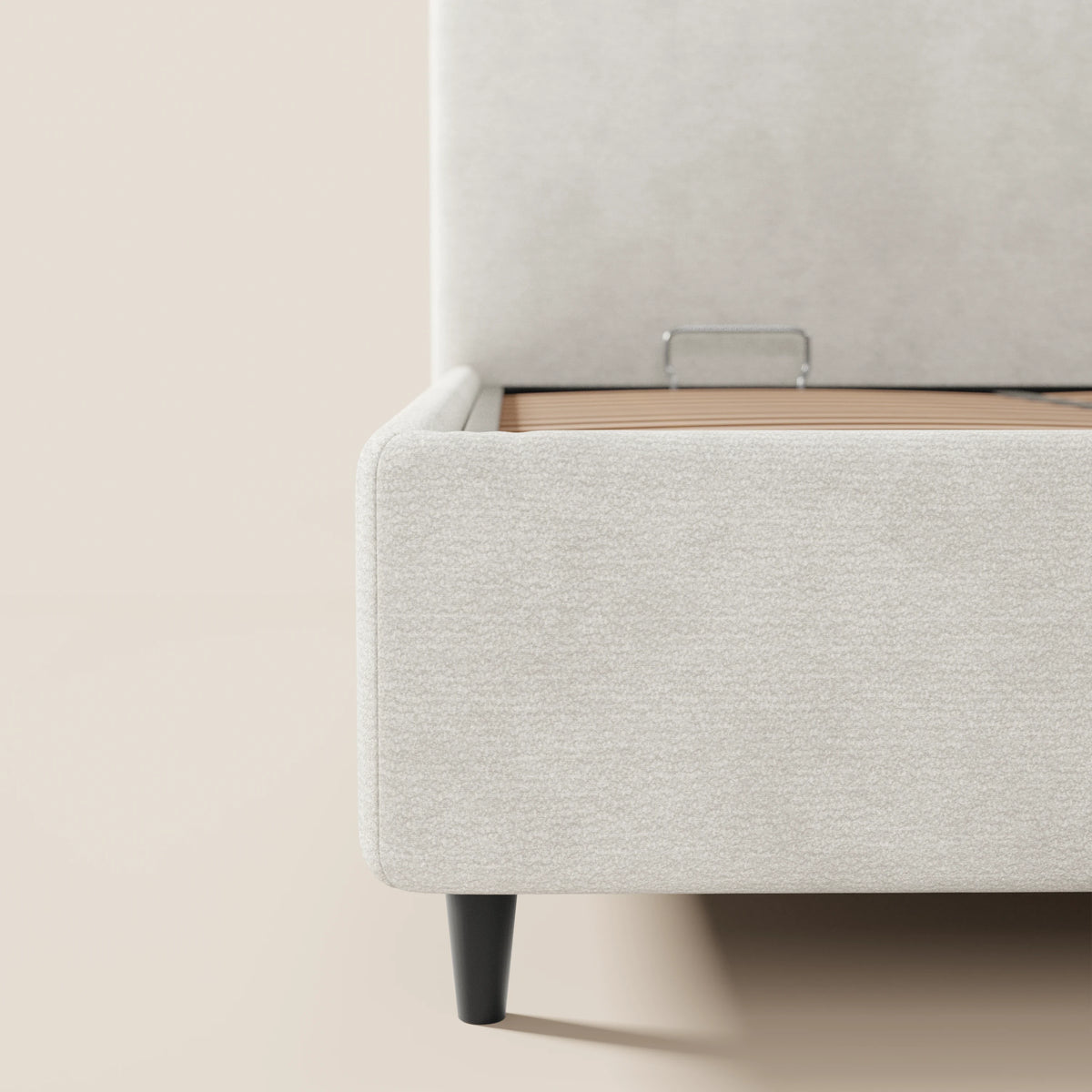 Primo piano del letto KAELOS minimal imbottito di Letti.store in ciniglia beige chiaro, che mette in risalto la base contenitiva, le gambe alte e affusolate di colore nero e la testiera arrotondata, esaltando le morbide texture su uno sfondo neutro.