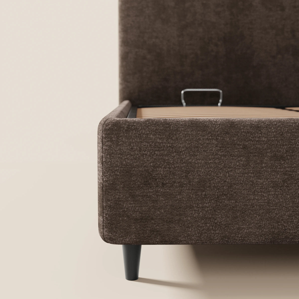 Il primo piano del letto imbottito KAELOS minimal di Letti.store ne mette in risalto il rivestimento in ciniglia marrone scuro, le gambe alte nere, la testiera arrotondata e la base a doghe in legno chiaro su uno sfondo beige neutro.
