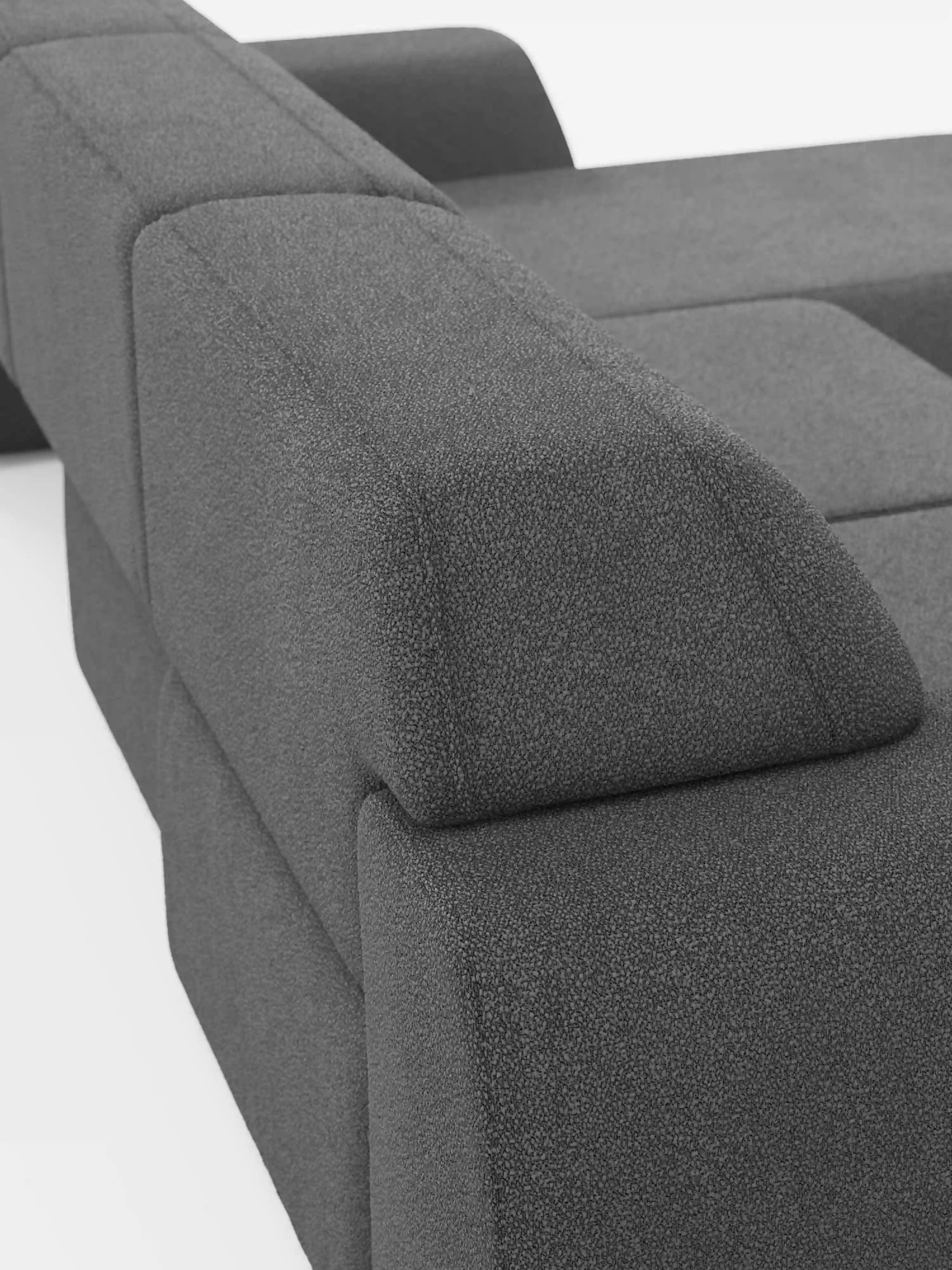 Primo piano del divano angolare Orbit con penisola reversibile e tutte le sedute allungabili, rivestito in tessuto smacchiabile effetto cotone T33 di divitt.sbs, caratterizzato da moderni cuscini geometrici grigio scuro e ampi braccioli che risaltano sullo sfondo bianco. Le linee pulite e il design minimalista mettono in risalto il rivestimento in tessuto di alta qualità, morbido e dalla trama ricca, di questo lussuoso divano componibile.