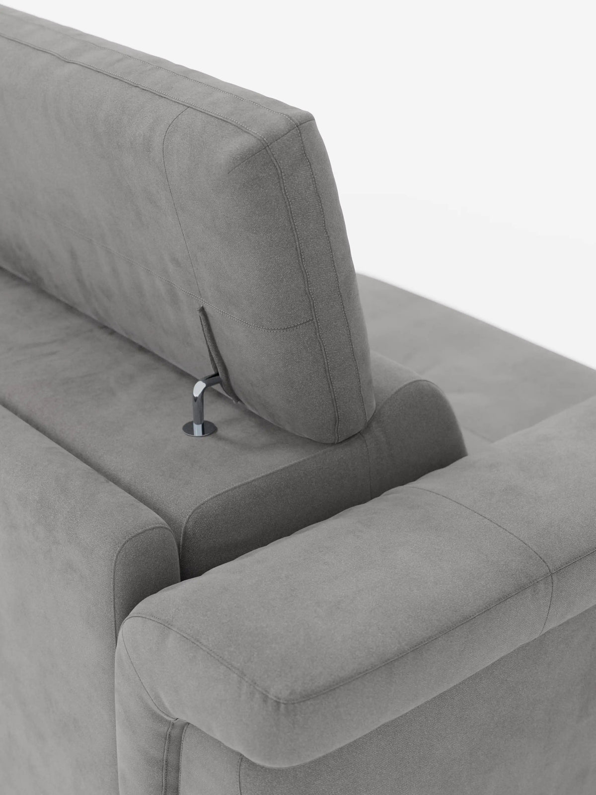 Primo piano del divano letto di design Capri di divitt.sbs, caratterizzato da un moderno angolo grigio con poggiatesta reclinabili fissati tramite eleganti aste metalliche. Il raffinato tessuto effetto velluto smacchiabile T30 presenta una morbida consistenza simile alla pelle scamosciata ed è caratterizzato da cuciture lisce e pulite che incarnano la manifattura italiana. Lo sfondo bianco a tinta unita mette in risalto gli eleganti dettagli di design del divano e i suoi caratteristici piedini alti.
