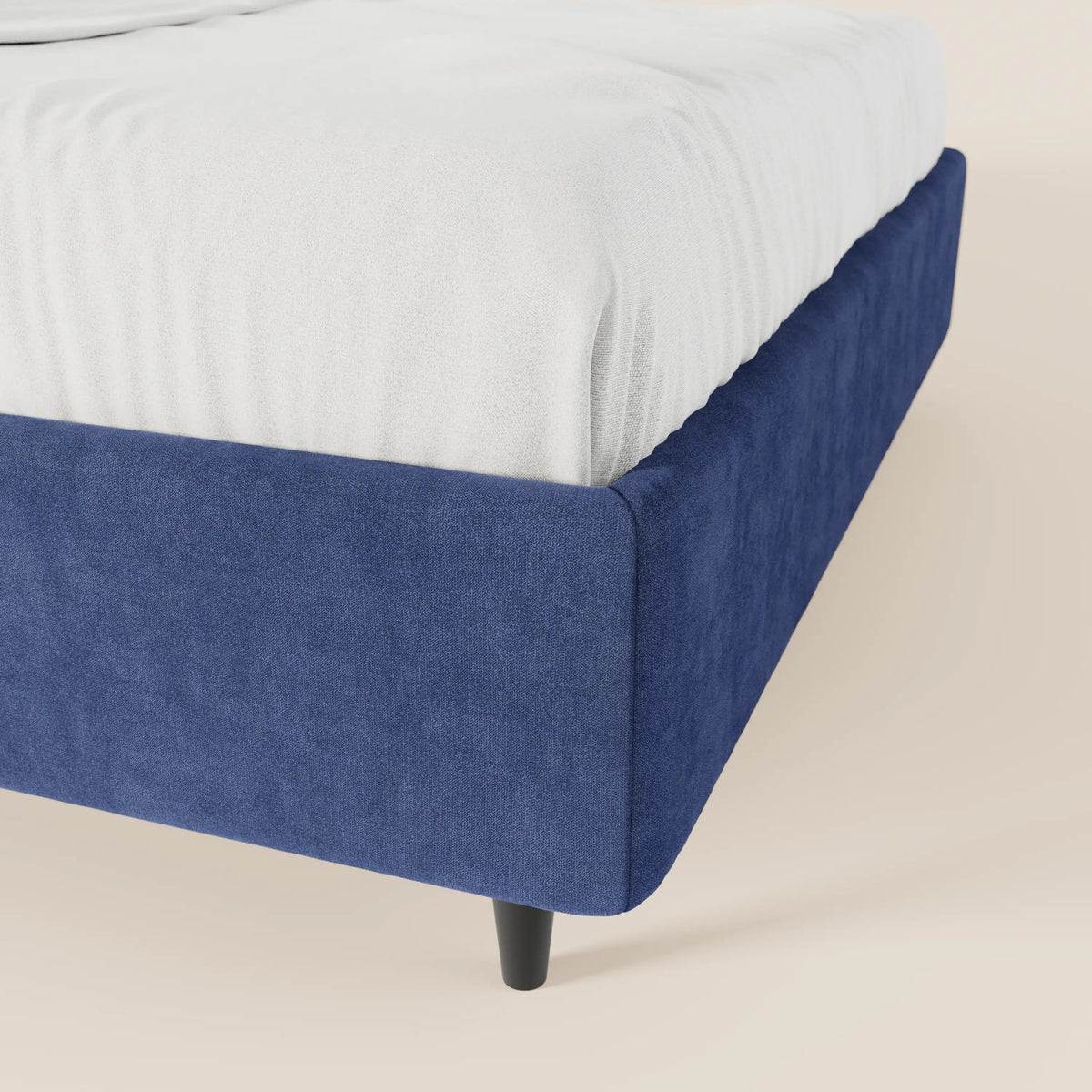Un primo piano del letto sommier imbottito ERON di Letti.store mette in risalto il suo tessuto impermeabile Oeko-Tex blu scuro, le gambe affusolate nere e il lenzuolo bianco ben stirato, il tutto su uno sfondo beige chiaro a tinta unita.