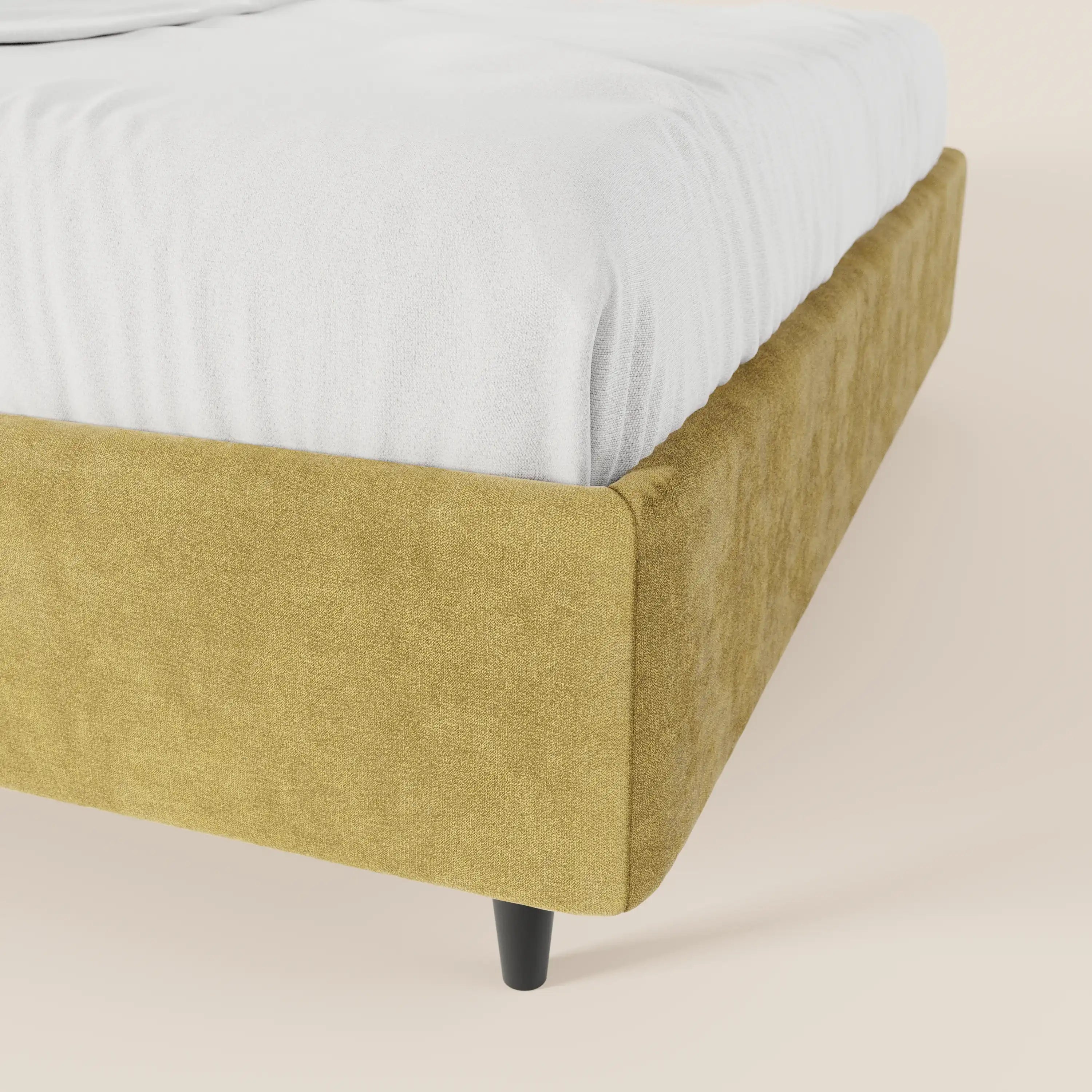 Primo piano del letto sommier imbottito ERON di Letti.store, caratterizzato da una struttura in tessuto impermeabile Oeko-Tex giallo senape, gambe corte nere a forma di cono e un materasso rivestito di lenzuola bianche su uno sfondo beige chiaro a tinta unita.