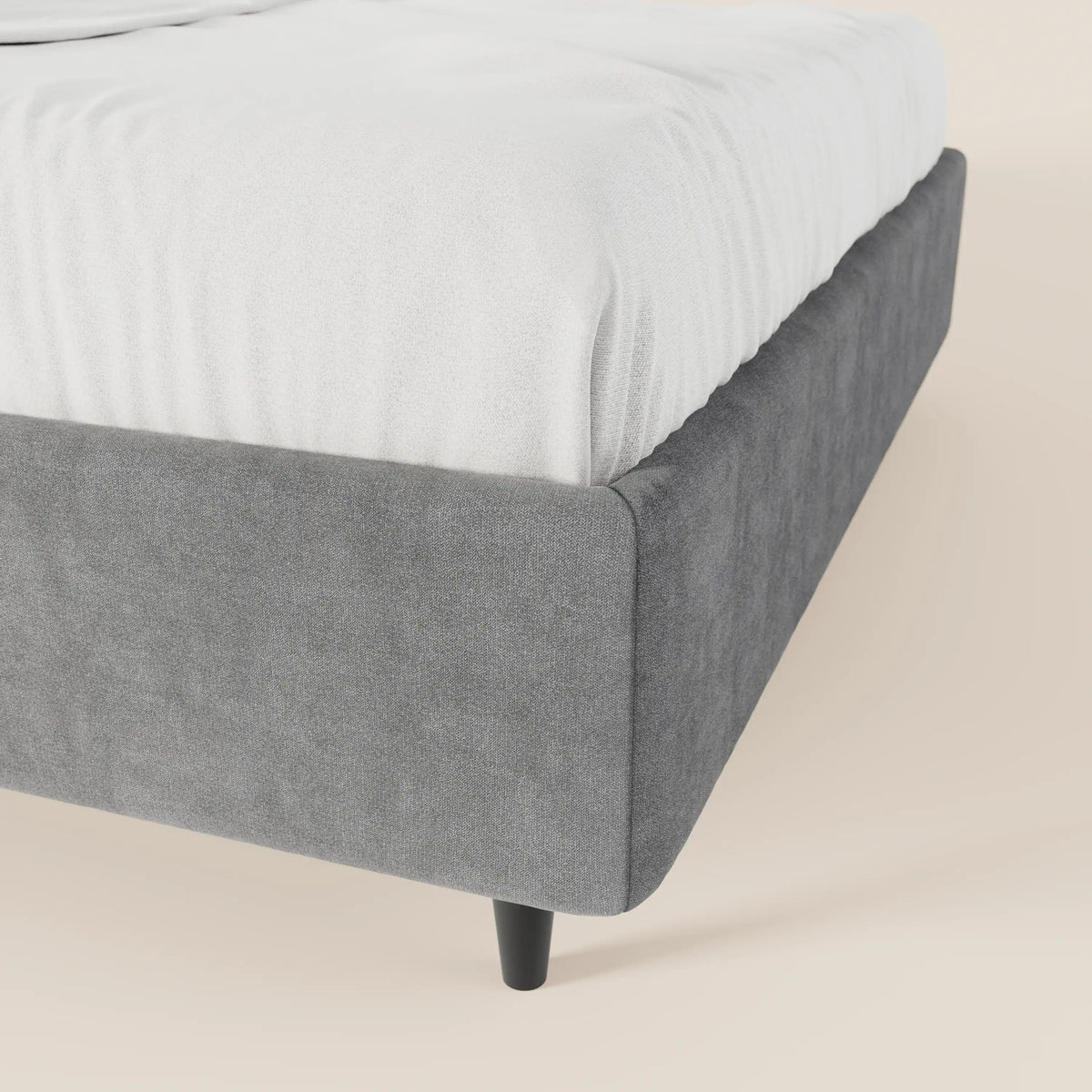 Primo piano del letto sommier imbottito con contenitore ERON di Letti.store, caratterizzato da una struttura in tessuto grigio impermeabile certificato Oeko-Tex e da gambe corte e affusolate di colore nero. Il letto dal design moderno è raffigurato con un lenzuolo bianco su uno sfondo beige.