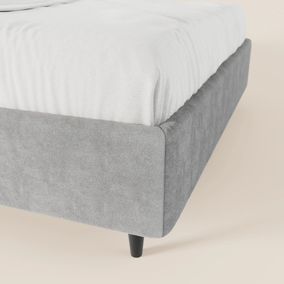 Un primo piano del letto sommier imbottito ERON di Letti.store mette in risalto il suo tessuto impermeabile Oeko-Tex grigio chiaro, i bordi arrotondati, le gambe affusolate nere e la biancheria da letto bianca. Uno sfondo neutro esalta il suo fascino minimalista e moderno.
