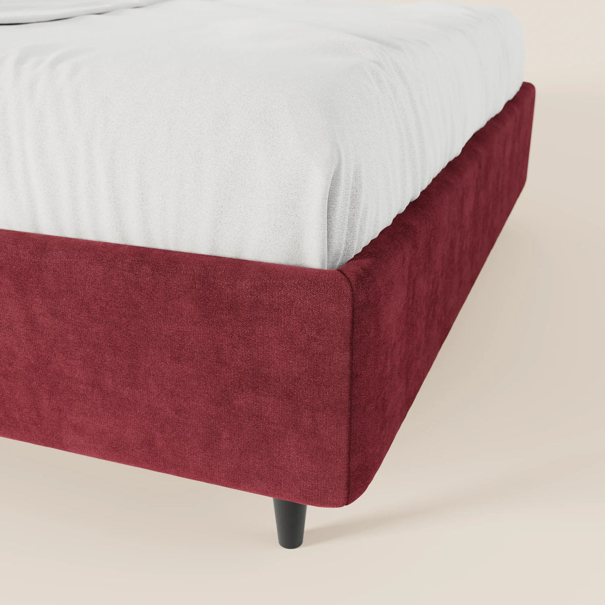 Primo piano del letto sommier imbottito ERON di Letti.store, caratterizzato da un tessuto impermeabile rosso intenso certificato Oeko-Tex e da gambe affusolate nere. Il materasso, rivestito con lenzuola bianche, si staglia su uno sfondo beige, creando un look pulito e minimalista.