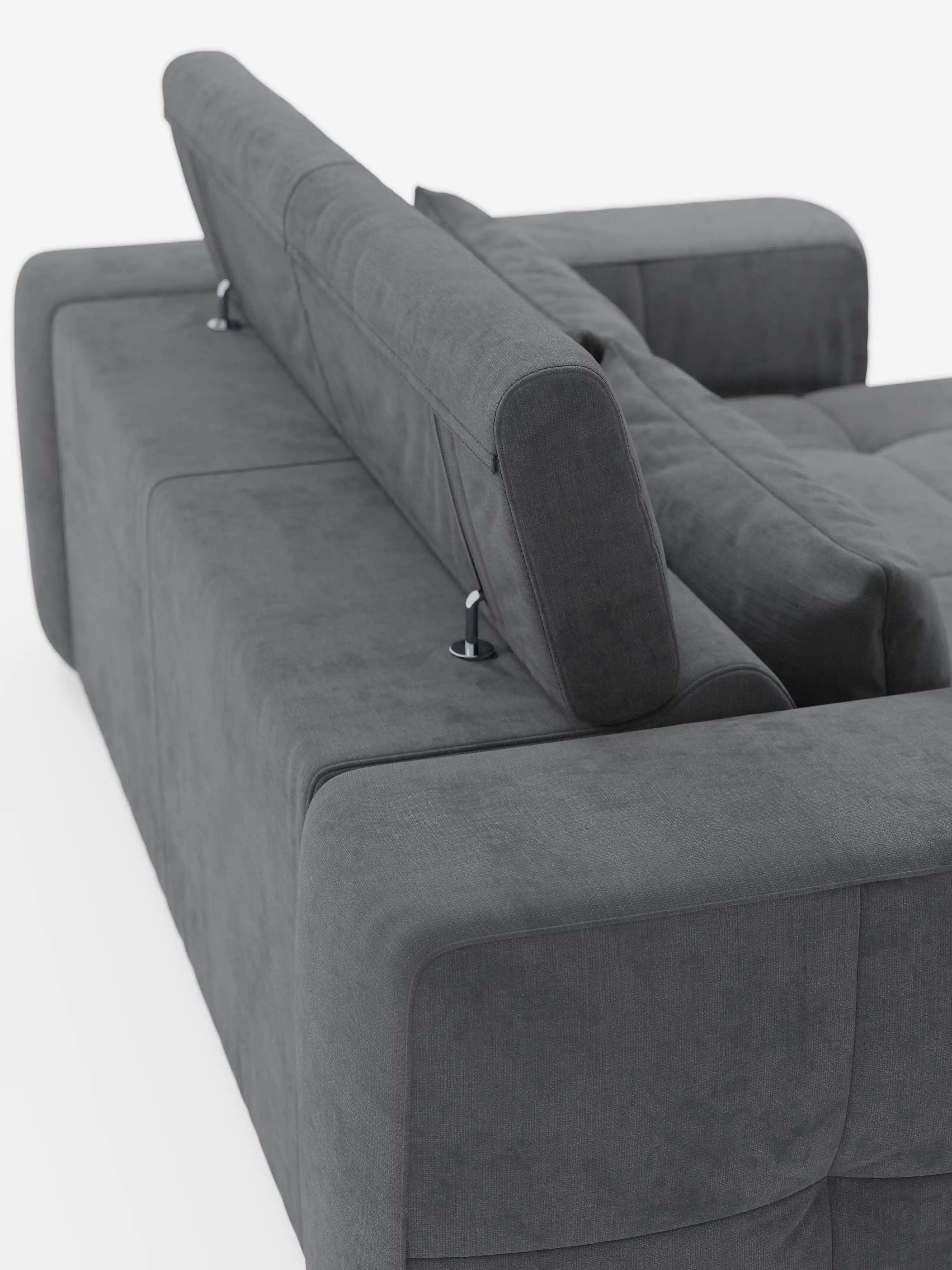 Un divano Monarch grigio scuro con funzione relax elettrica per l’allungamento delle sedute e poggiatesta reclinabile, rivestito in morbido tessuto smacchiabile T31 di divitt.sbs, visto di sbieco dall’angolo posteriore. Il rivestimento appare morbido e questo moderno divano componibile presenta un design squadrato con braccioli spessi e supporti in metallo per i poggiatesta regolabili.