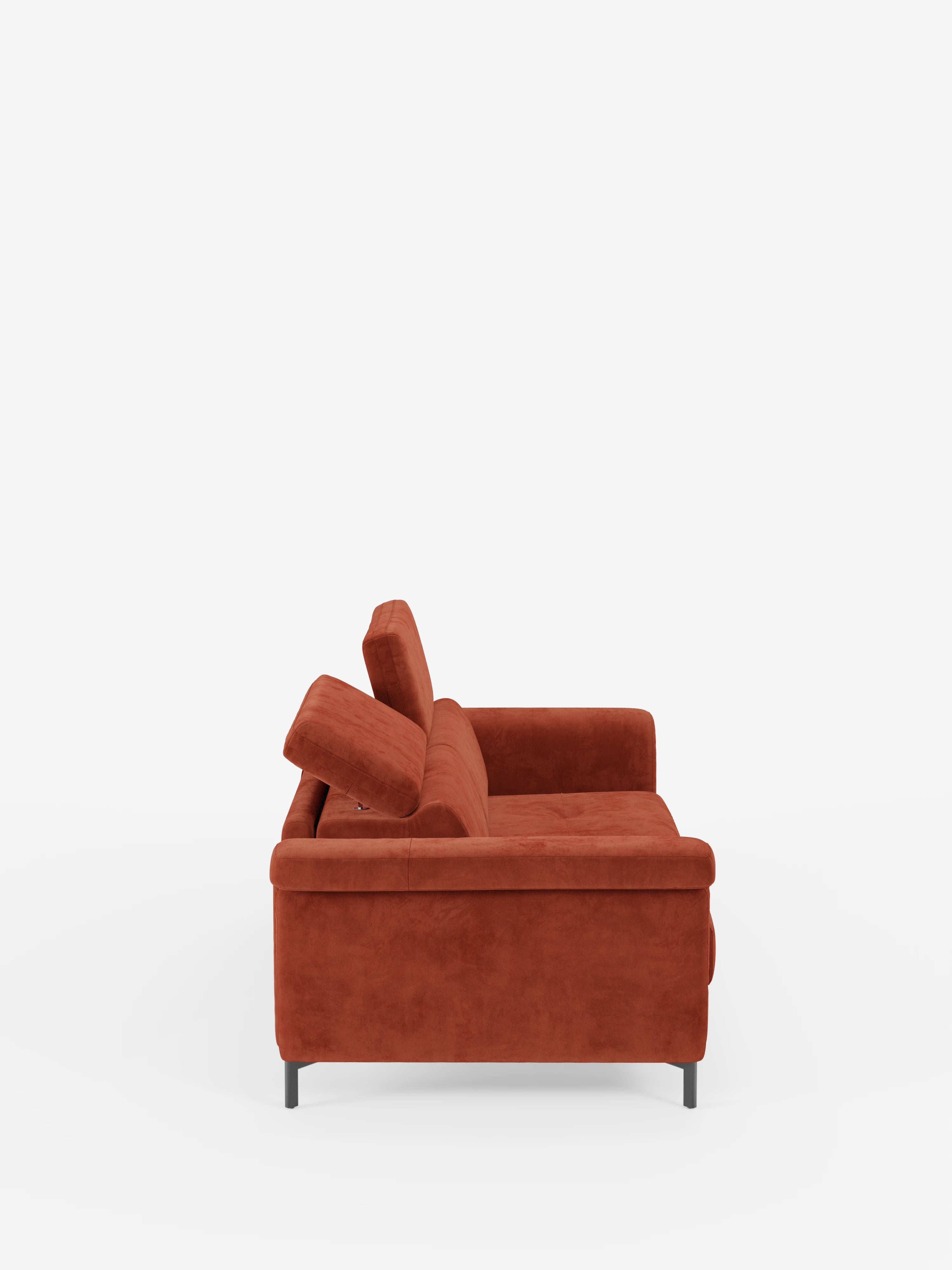Vista laterale del divano letto di design Capri di divitt.sbs, rivestito in raffinato tessuto effetto velluto smacchiabile T30 di colore rosso ruggine, caratterizzato da linee pulite, morbidi cuscini, sottili piedini alti in metallo nero e poggiatesta reclinabili regolabili, il tutto su uno sfondo bianco a tinta unita.