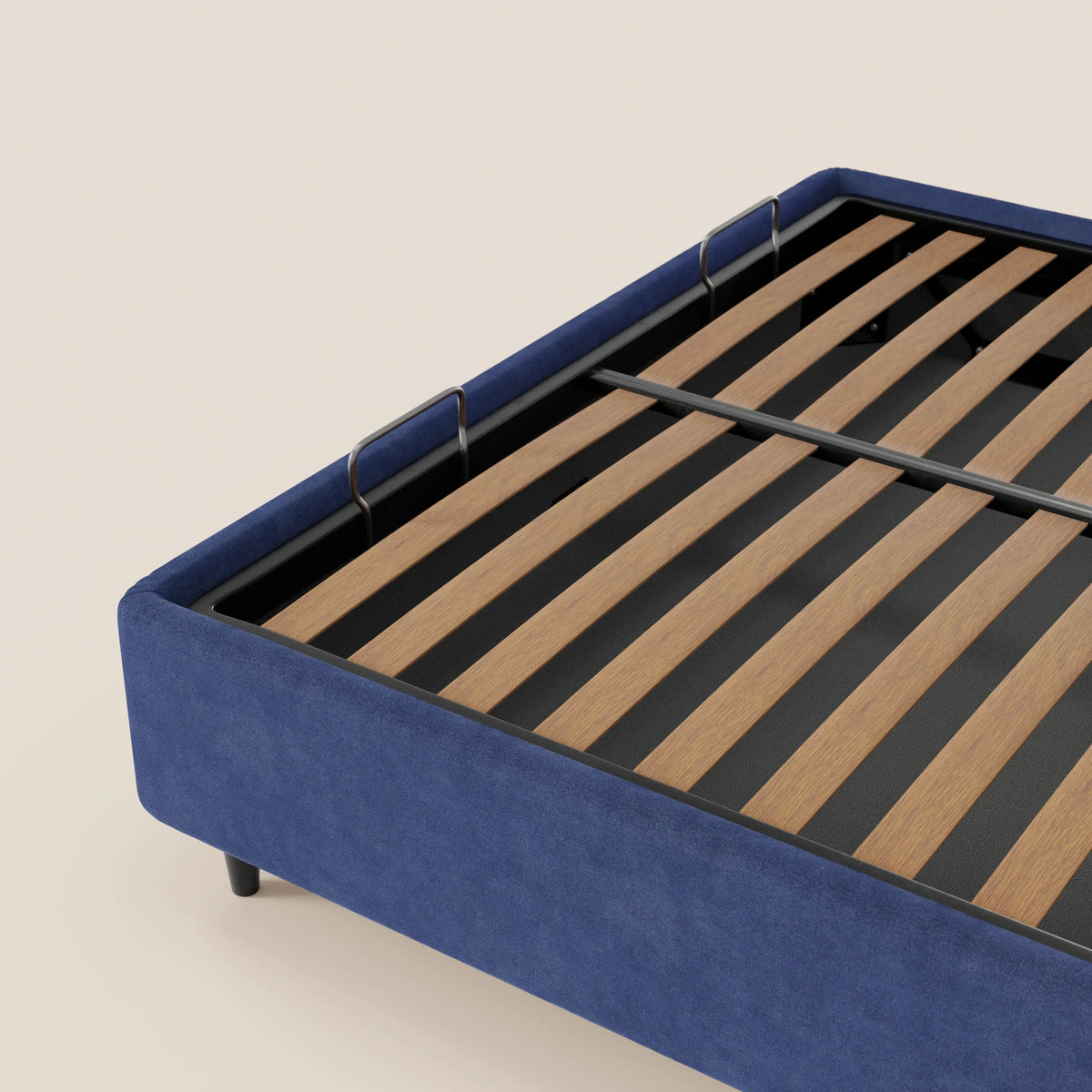 Un primo piano del letto sommier imbottito con contenitore ERON di Letti.store, caratterizzato da una base in tessuto blu impermeabile certificato Oeko-Tex, gambe nere, doghe in legno e due fermamaterasso in metallo nero. Lo sfondo è beige chiaro.