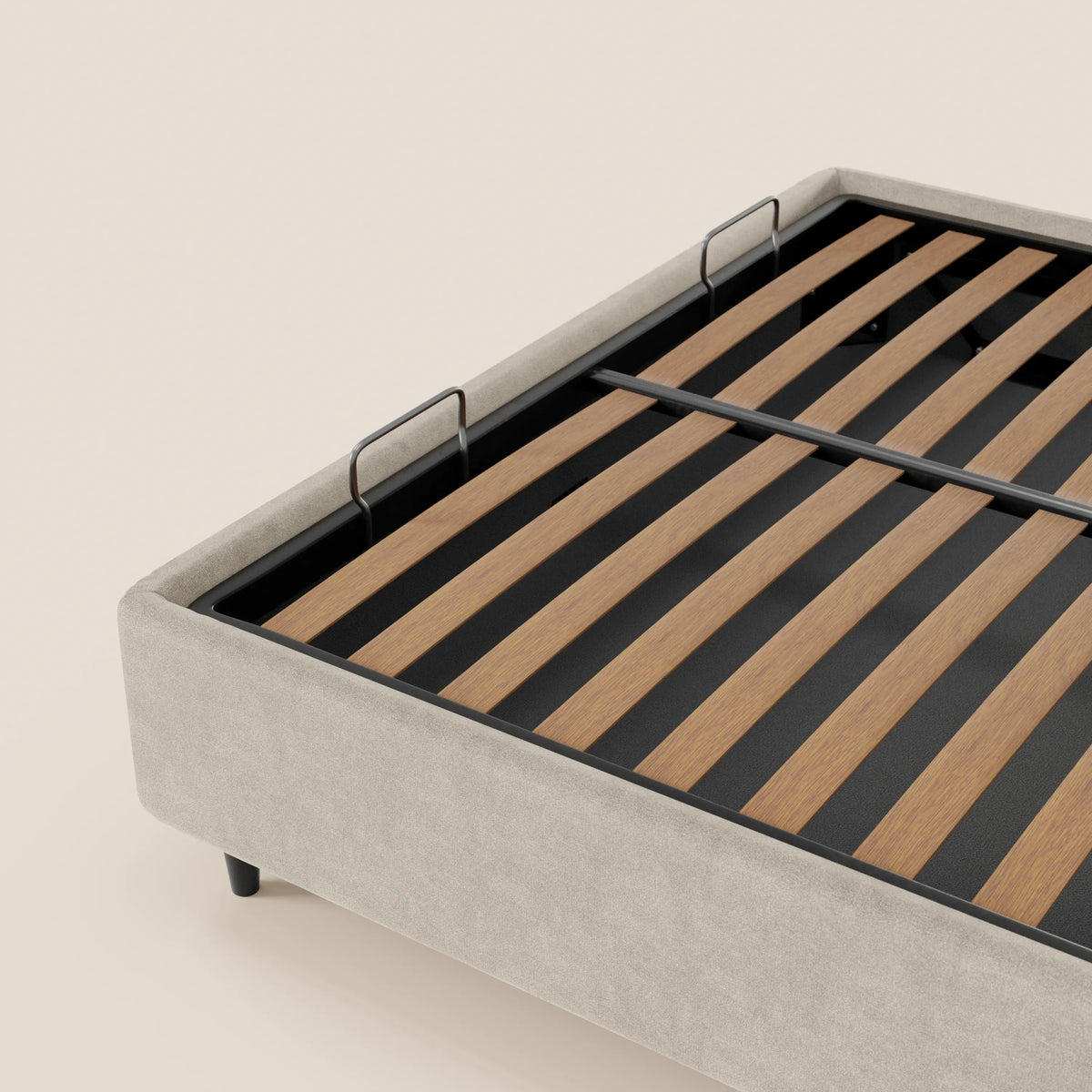 Un primo piano del letto sommier imbottito con contenitore ERON di Letti.store mette in risalto il suo tessuto impermeabile Oeko-Tex color beige chiaro, i supporti in metallo nero e le doghe in legno con due staffe verticali, il tutto su uno sfondo morbido color avorio.