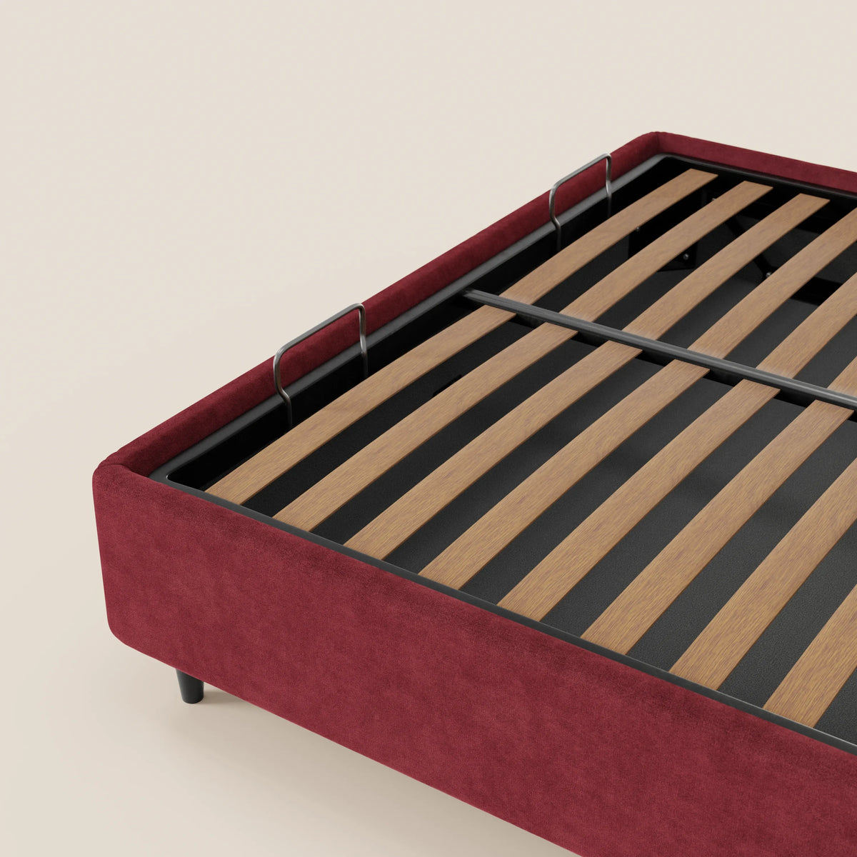 Una vista angolare del letto sommier imbottito con vano contenitore ERON di Letti.store, caratterizzato da una base in tessuto rosso impermeabile certificato Oeko-Tex, doghe in legno, sponde laterali in metallo nero e gambe corte nere su uno sfondo beige.