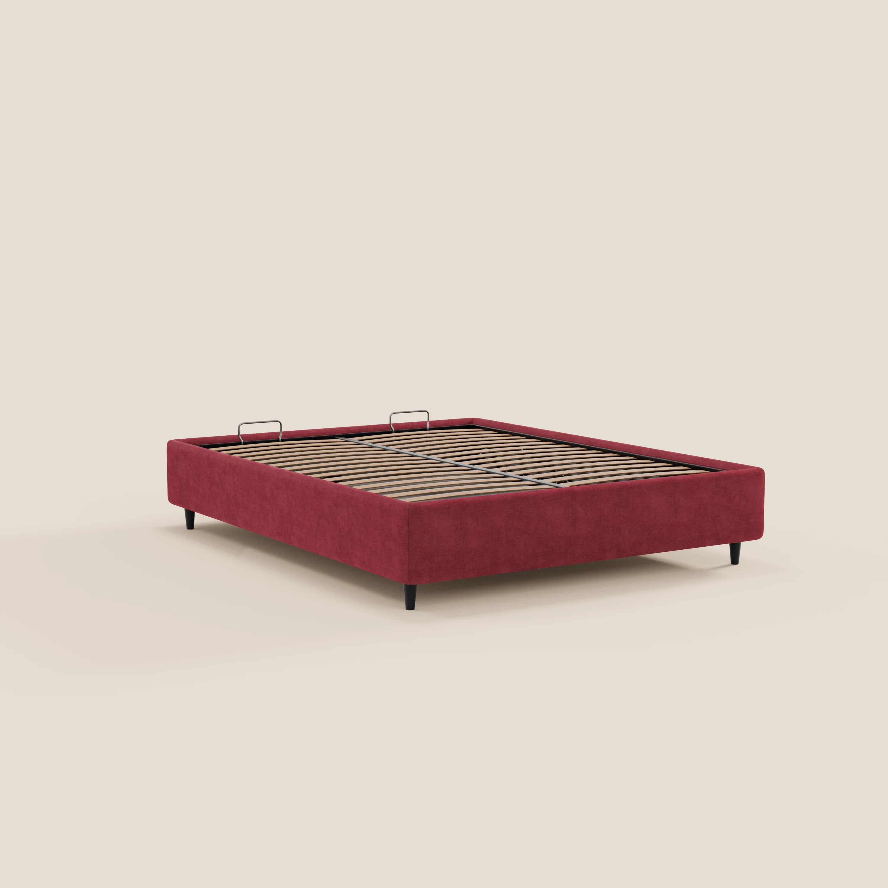 Il letto sommier imbottito ERON di Letti.store presenta una base in tessuto rosso impermeabile certificato Oeko-Tex, gambe nere, doghe in legno e due supporti metallici per il materasso nella zona della testata. È presentato senza materasso né biancheria da letto su uno sfondo beige.