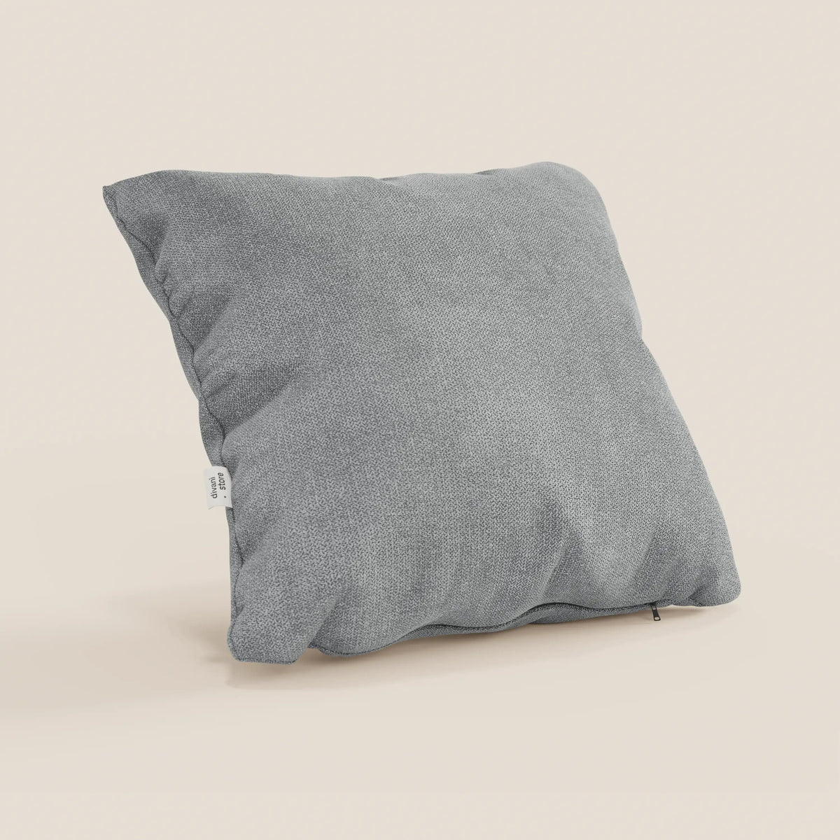Il cuscino Destiny di divitt.sbs, 45x45 cm, in morbido tessuto impermeabile T02 grigio chiaro con una sottile trama intrecciata e una targhetta laterale bianca, si staglia su uno sfondo beige chiaro. Federa lavabile.