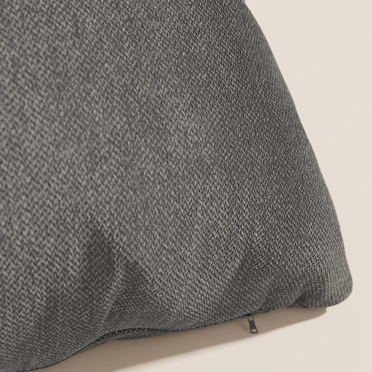 Un primo piano del cuscino Sogno di divitt.sbs in tessuto antracite SMACCHIABILE T05 mostra la sua trama morbida e sottile e una discreta cerniera nera, con una parte di questo elegante cuscino su uno sfondo beige chiaro.