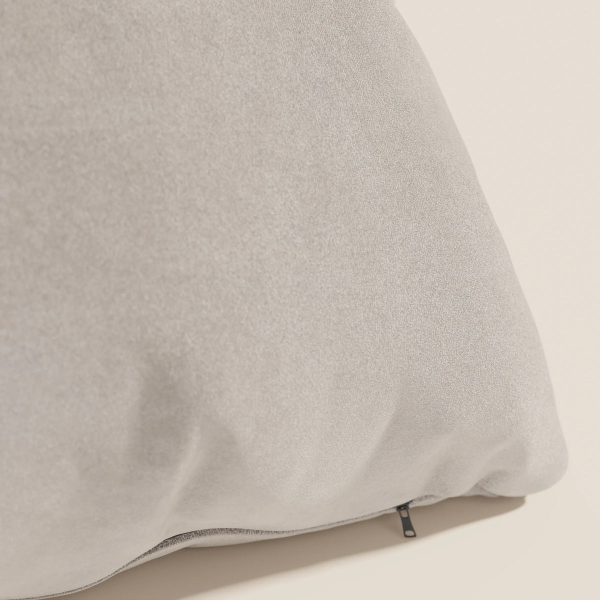 Primo piano del cuscino Jazz 45x45 di divitt.sbs, in microfibra tecnica smacchiabile T11 tortora. Il cuscino grigio chiaro poggia su una superficie beige, con una piccola cerniera nera sul fondo che lascia intravedere un rivestimento sfoderabile.