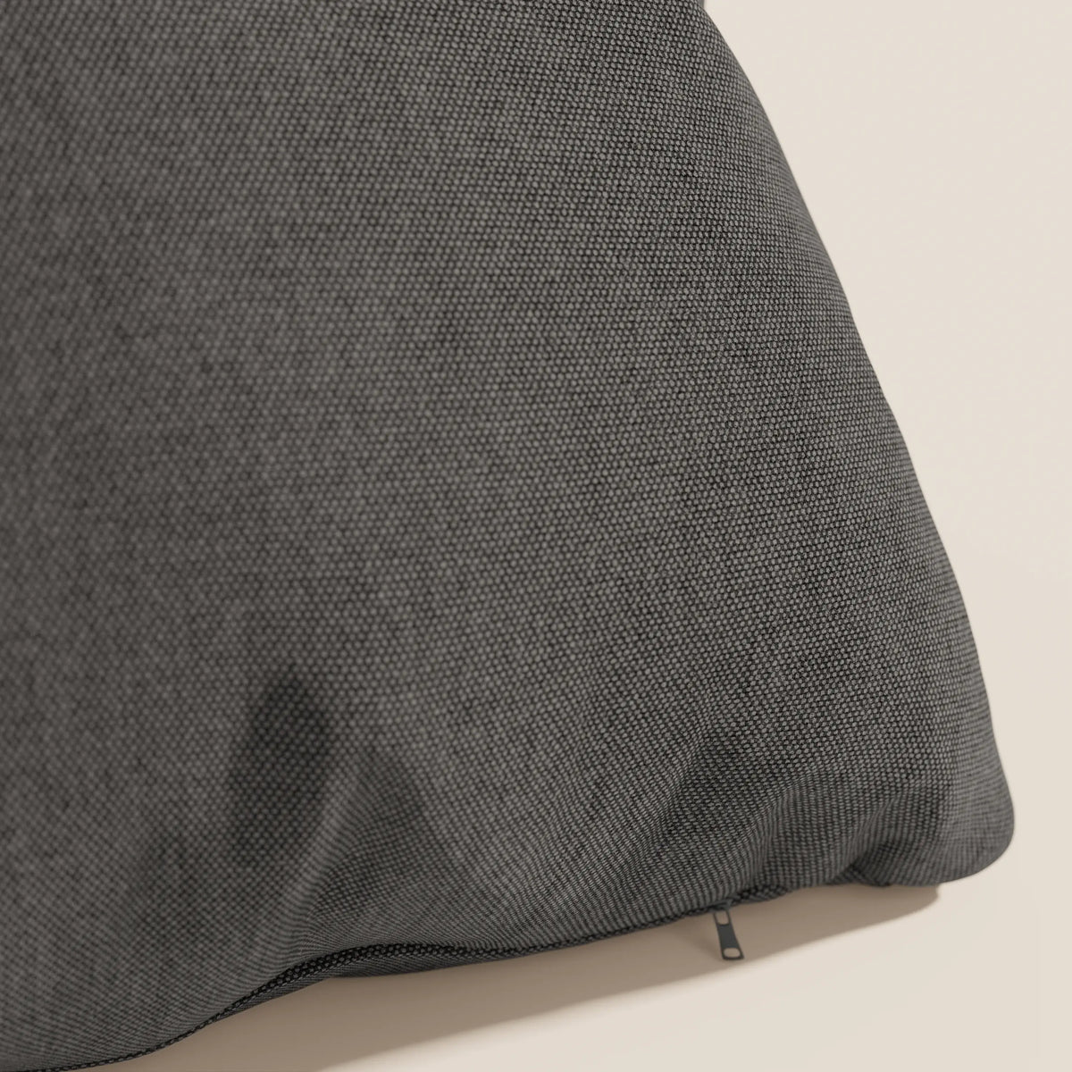 Primo piano del cuscino Honey 45x45 di divitt.sbs in tessuto simil cotone impermeabile T13 antracite, su sfondo beige. Sul bordo è visibile una piccola cerniera nera, con una debole macchia scura sulla fodera inferiore lavabile.