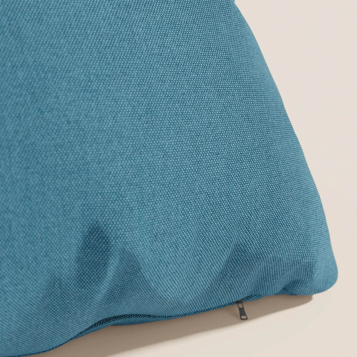 Primo piano del cuscino Honey 45x45 di divitt.sbs in tessuto simil cotone impermeabile T13 azzurro, angolato su uno sfondo beige chiaro. La cerniera parzialmente visibile della fodera lavabile ne rivela la trama fine e leggermente rugosa.