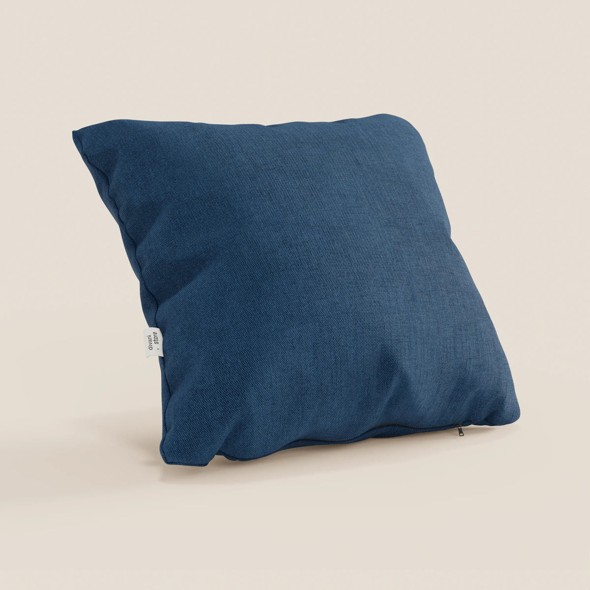 Il cuscino Honey di divitt.sbs, in tessuto blu simil cotone impermeabile T13 (45x45), è posizionato in verticale su uno sfondo bianco sporco, con una piccola etichetta bianca sul lato e una cerniera a vista per la fodera lavabile.