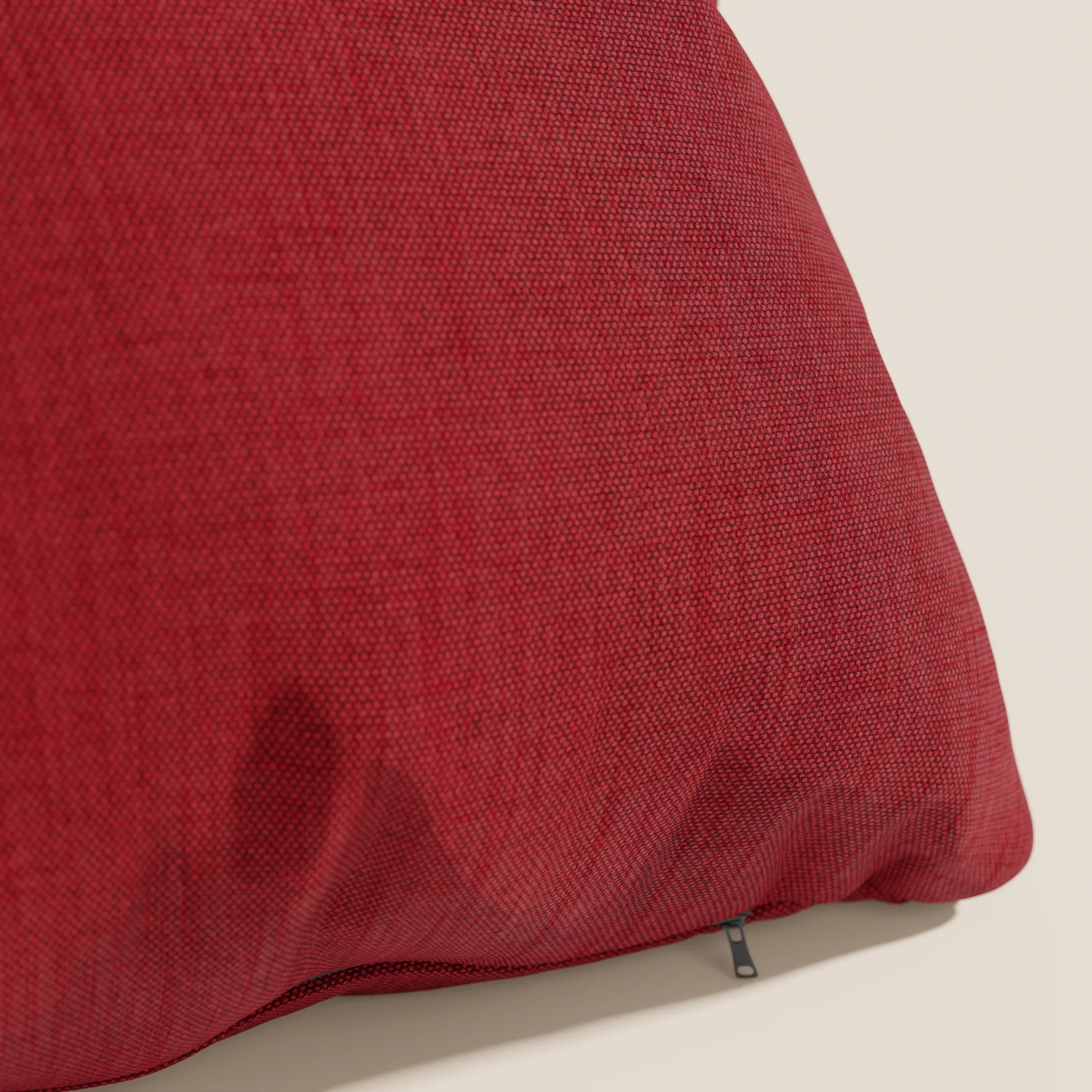 Un primo piano del cuscino Honey 45x45 impermeabile in rosso di divitt.sbs, realizzato in tessuto similcotone T13 rosso, è mostrato su uno sfondo beige chiaro con una cerniera nera a vista che ne evidenzia l'aspetto felpato.