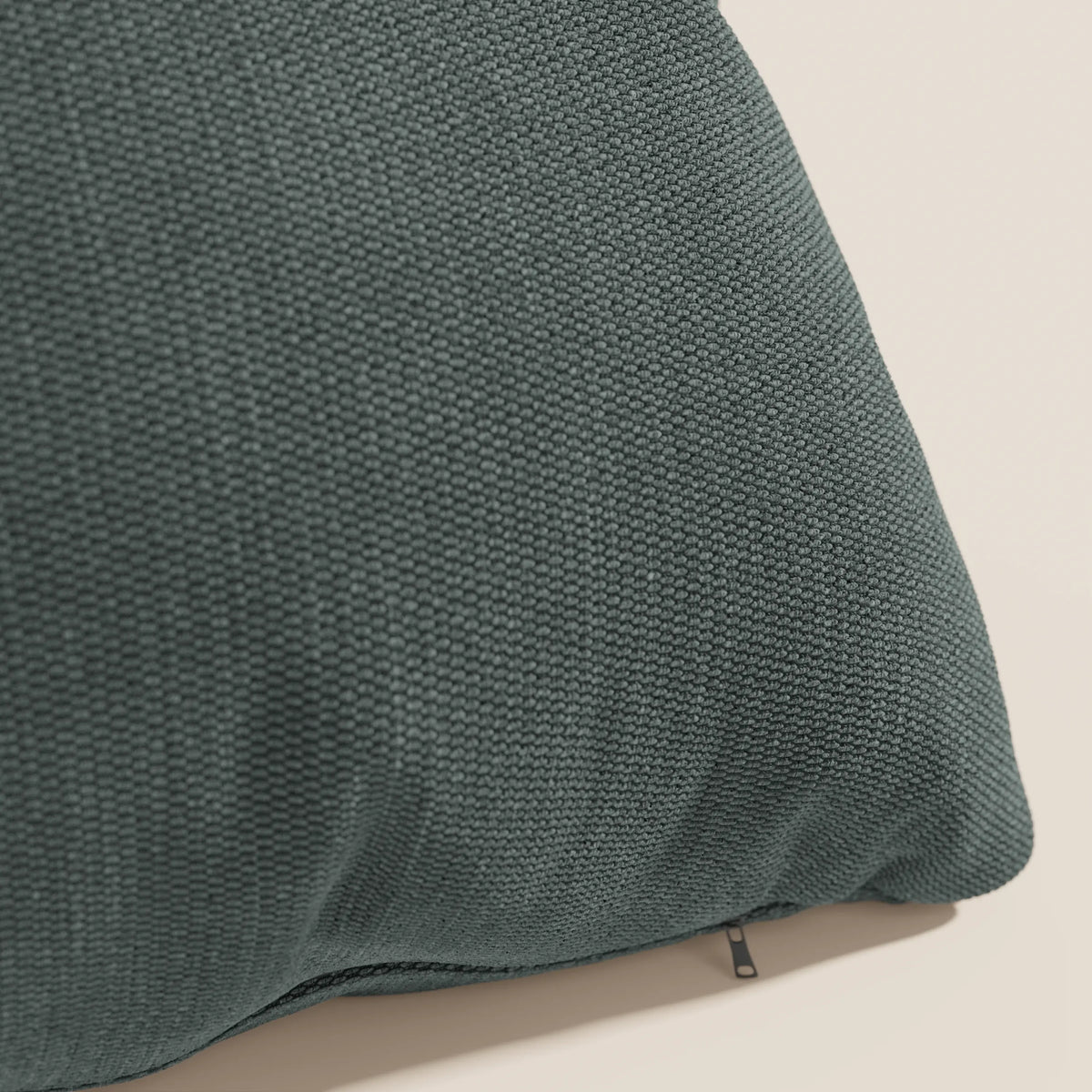 Primo piano del cuscino Miami 45x45 cm di divitt.sbs in verde T14, realizzato in morbido tessuto impermeabile. Il rivestimento sfoderabile è dotato di una cerniera a vista. Solo una parte del cuscino testurizzato è mostrata su uno sfondo a tinta unita.