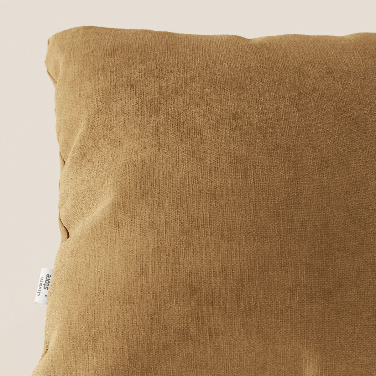 Primo piano del cuscino Bolero quadrato marrone di divitt.sbs, realizzato in morbido tessuto T31 antimacchia, impermeabile e non restringente. Una piccola etichetta bianca si trova sulla cucitura laterale. Lo sfondo chiaro evidenzia la consistenza del cuscino.