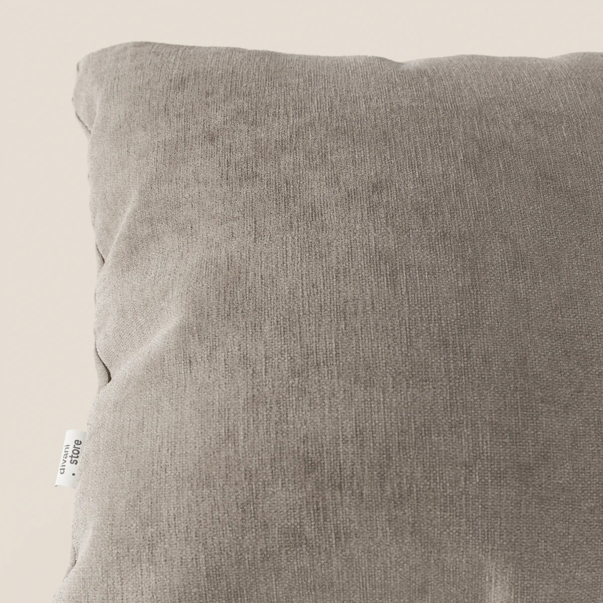 Primo piano dell'angolo superiore sinistro di Bolero cuscino di divitt.sbs in morbido, smacchiabile, impermeabile e irrestringibile tessuto T31, con etichetta in tessuto visibile sulla cucitura. Lo sfondo è un semplice beige chiaro. Viene mostrata solo una parte del cuscino.