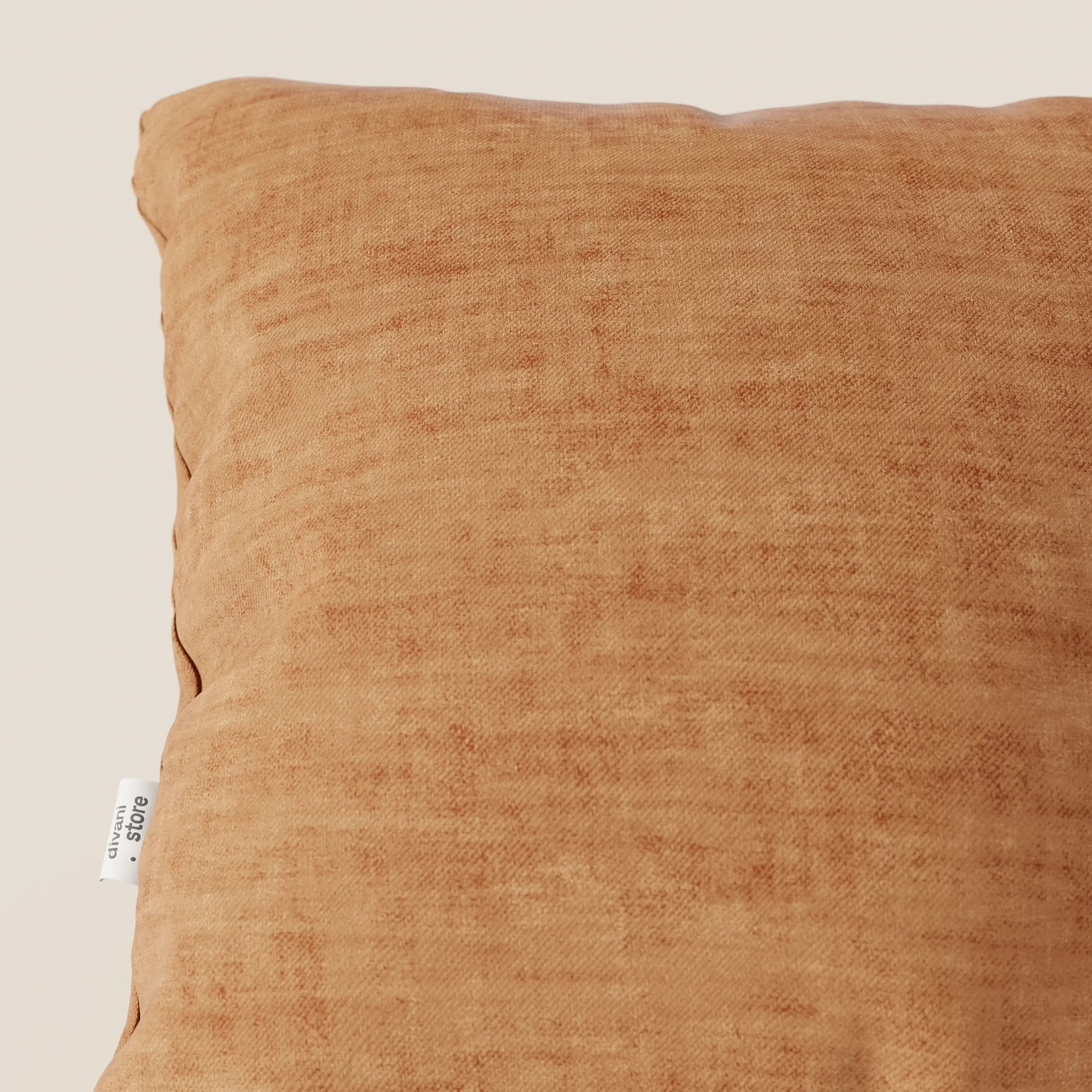 Primo piano del cuscino Sofia di divitt.sbs in velluto nuvolato T35 color ruggine con una texture sottile. Una targhetta in tessuto bianco con testo nero è cucita nella cucitura sinistra. Lo sfondo è un semplice beige chiaro.
