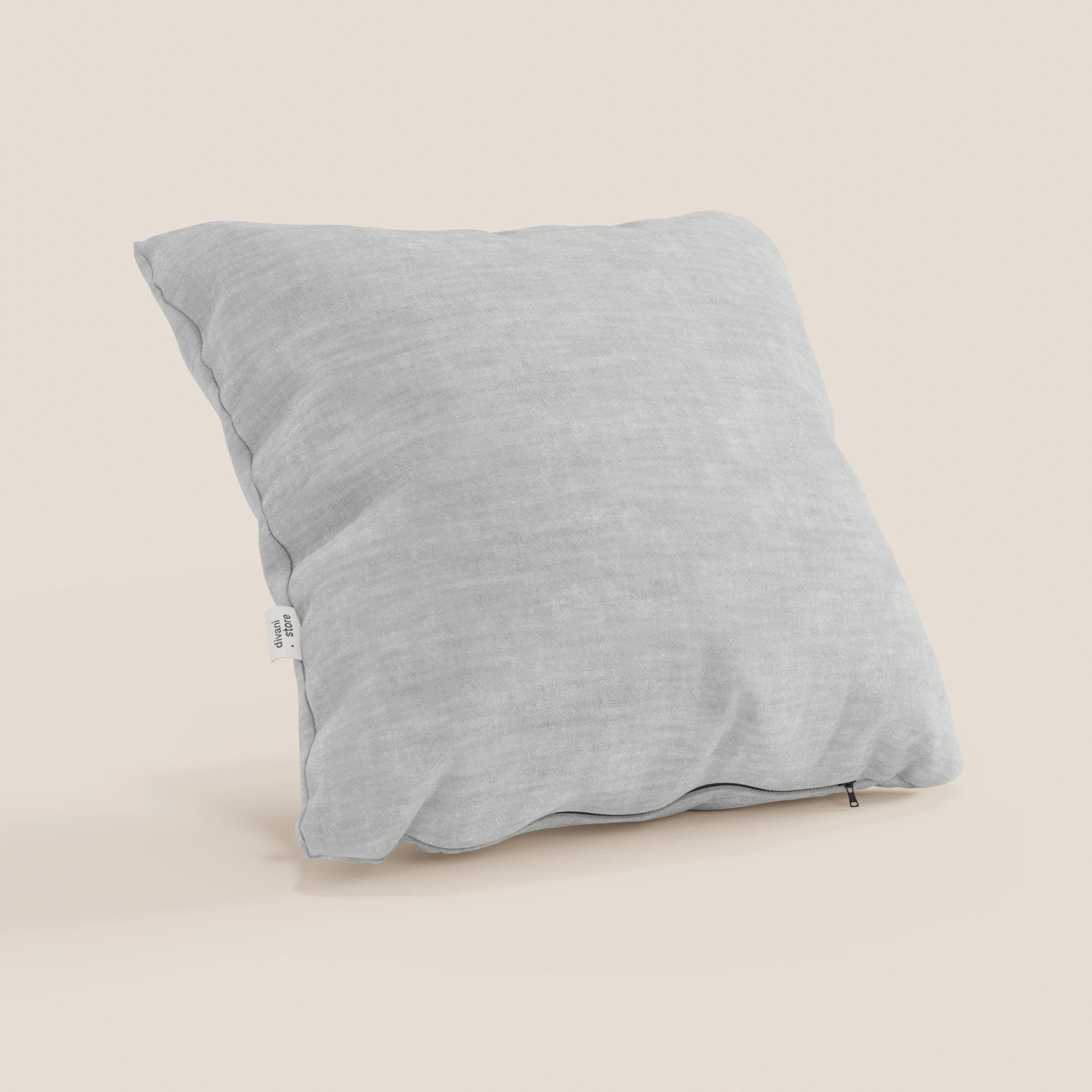 Il cuscino Sofia di divitt.sbs, di forma quadrata e di colore grigio chiaro, è realizzato in morbido velluto nuvolato impermeabile e antimacchia e poggia su una superficie beige chiaro. Sul bordo sono visibili una piccola etichetta bianca e un discreto tiretto per la cerniera.