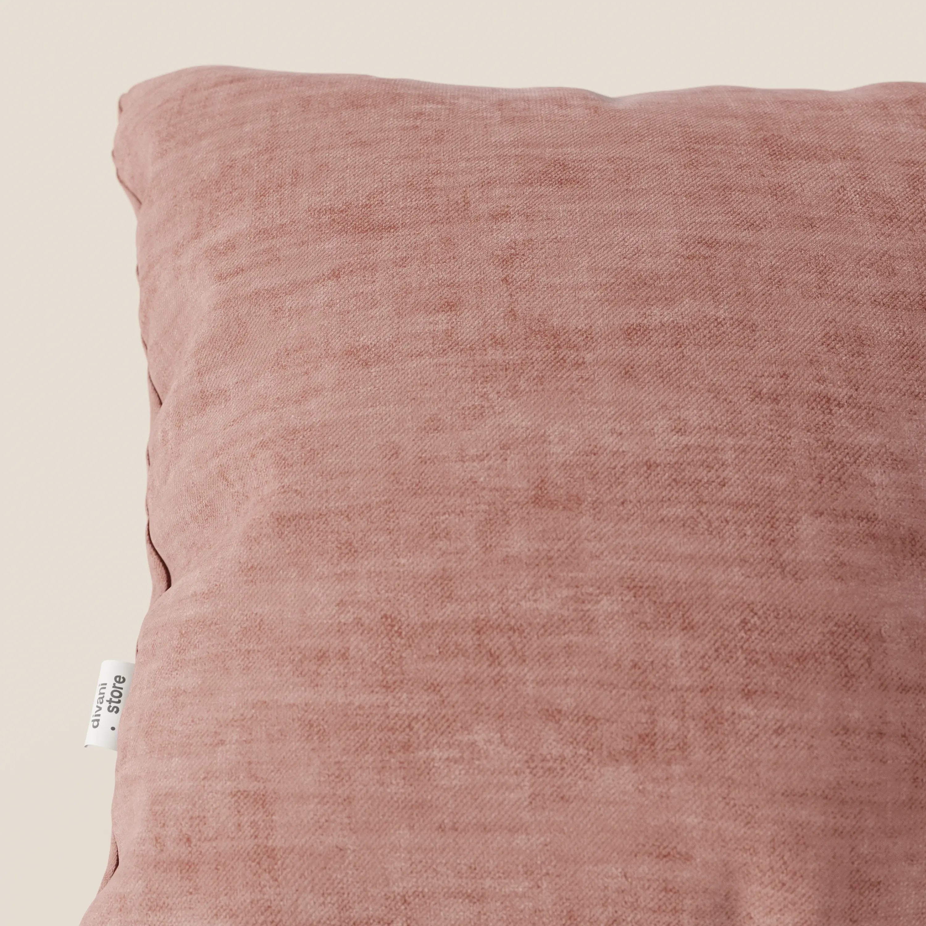 Primo piano del cuscino Sofia di divitt.sbs, in velluto Easy Clean T35 rosa tenue con texture screziata e etichetta bianca sul bordo sinistro, su uno sfondo crema chiaro.