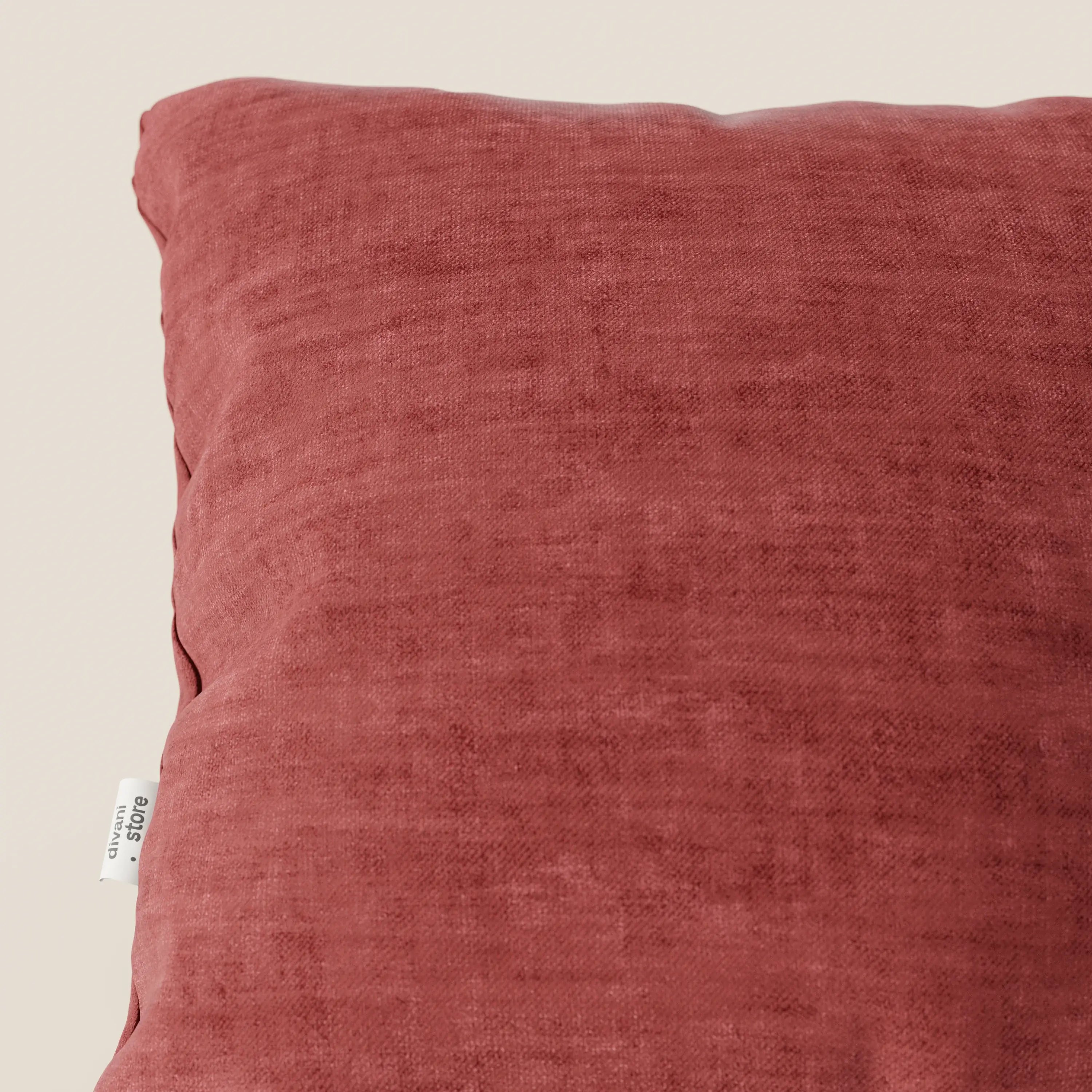 Primo piano del cuscino Sofia di divitt.sbs, in velluto nuvolato Easy Clean T35 lavabile e impermeabile rosso ruggine, su uno sfondo beige tinta unita. L'etichetta del tessuto è visibile sulla cucitura sinistra; il cuscino ha una consistenza morbida e vellutata.
