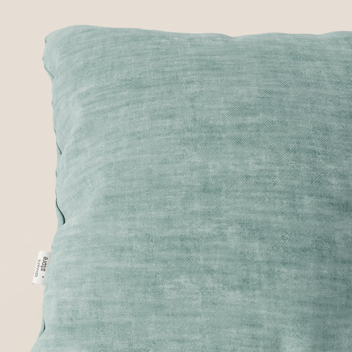 Primo piano del cuscino Sofia verde chiaro di divitt.sbs, realizzato in morbido velluto Easy Clean T35 impermeabile e antimacchia. Il cuscino quadrato presenta un'etichetta di tessuto visibile sul lato sinistro e poggia su uno sfondo neutro.