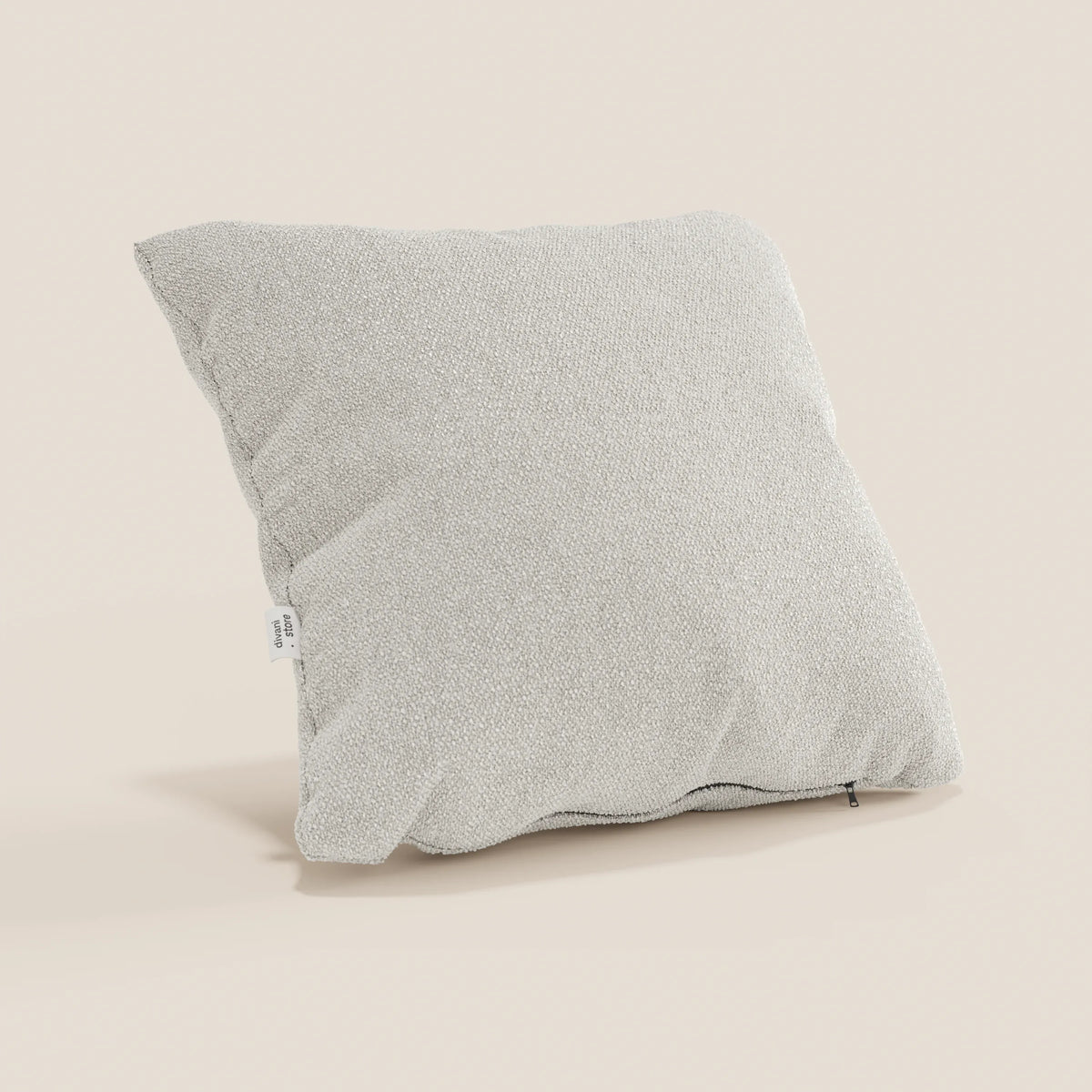 Un cuscino Lambada di divitt.sbs in tessuto T33 grigio chiaro, simil-cotone, antimacchia e impermeabile, poggia su uno sfondo beige, con un'etichetta bianca su una cucitura e una discreta cerniera lungo il bordo inferiore.