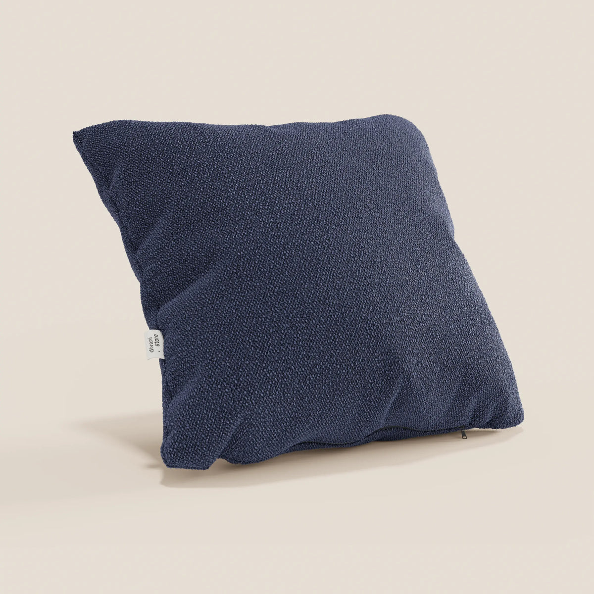 Il cuscino Lambada di divitt.sbs, di forma quadrata e di colore blu navy, si trova su uno sfondo beige chiaro. Realizzato in fresco tessuto T33 antimacchia e impermeabile, dall'aspetto naturale, è caratterizzato da un design minimalista con una piccola etichetta bianca sul lato.