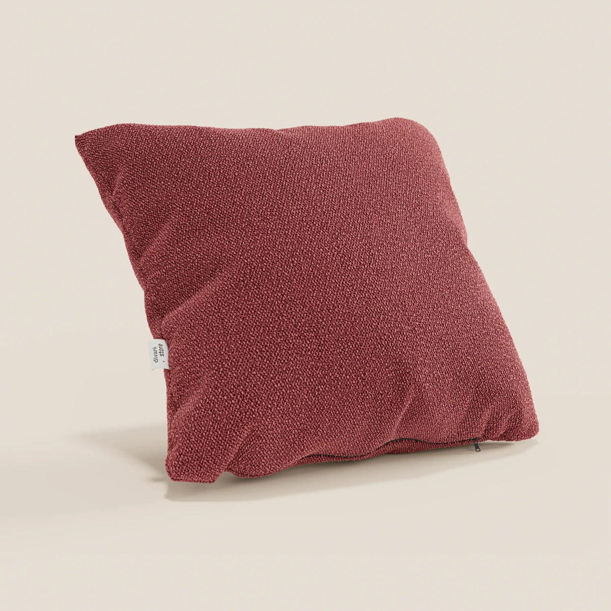 Un cuscino Lambada rosso quadrato di divitt.sbs, realizzato in tessuto naturale simil-cotone T33 lavabile e impermeabile, sta in piedi su uno sfondo beige chiaro con una piccola etichetta bianca su un lato.