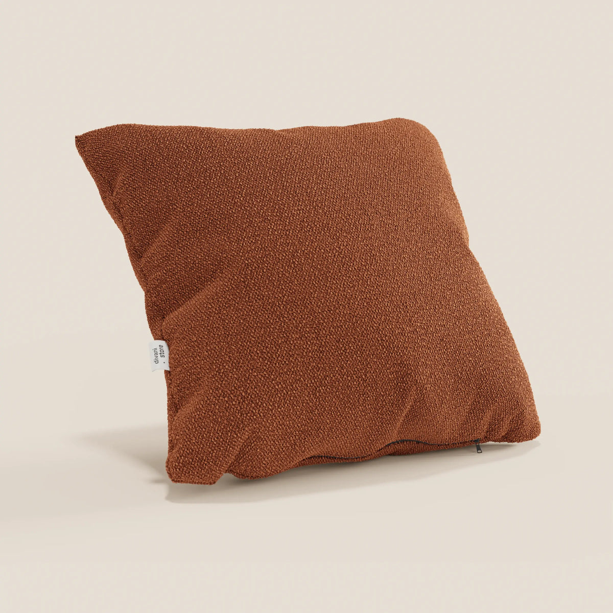 divitt.sbs presenta un cuscino Lambada quadrato color ruggine su uno sfondo beige chiaro. Realizzato in tessuto naturale simil-cotone (T33), fresco, lavabile e impermeabile, presenta una superficie strutturata e una piccola etichetta laterale bianca.