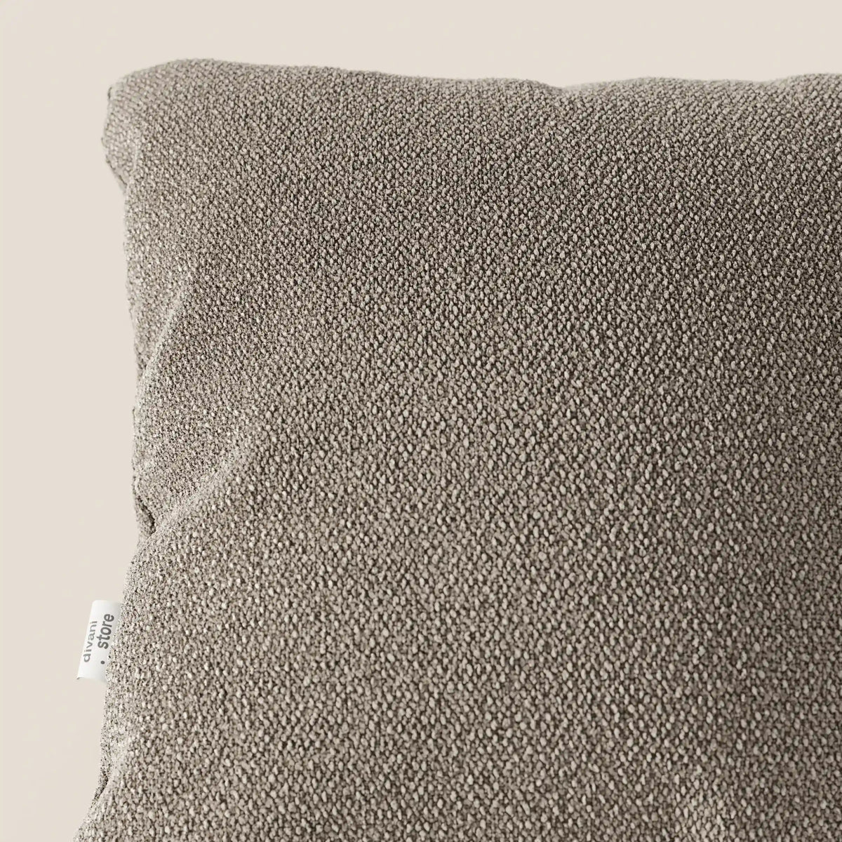 Primo piano del cuscino Lambada di divitt.sbs in grigio tortora, realizzato in fresco tessuto T33 simile al cotone naturale, resistente alle macchie e all'acqua. Una piccola etichetta bianca è visibile sul cuscino quadrato morbido e strutturato su uno sfondo neutro.