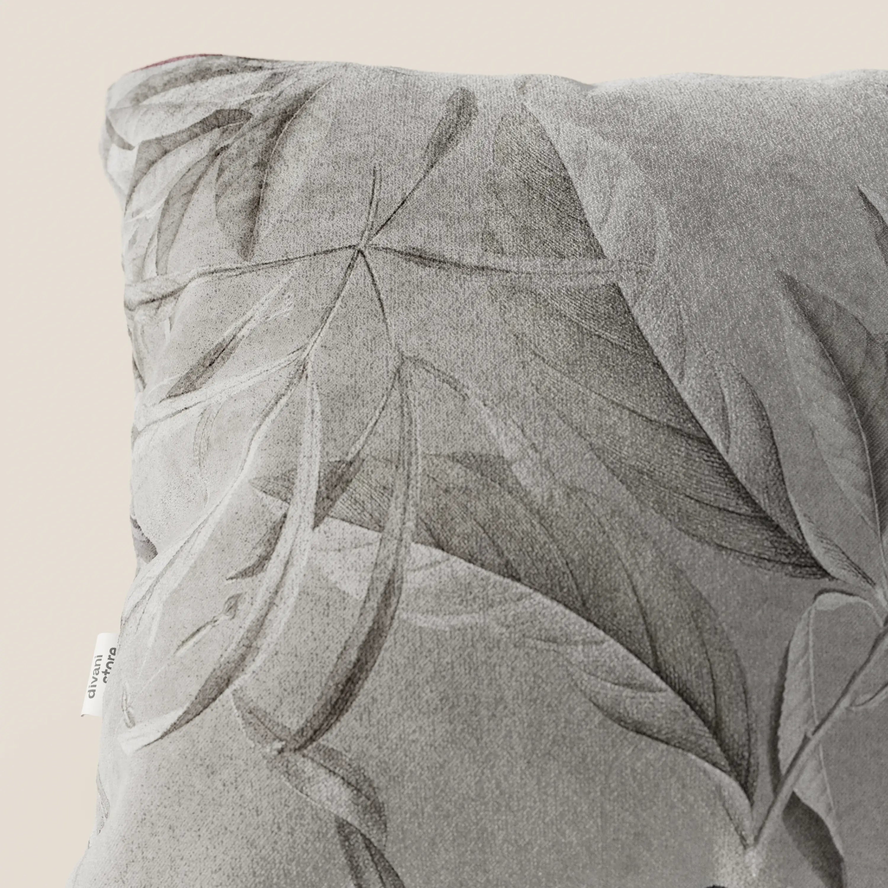 Un primo piano della collezione Lemon elegante di cuscini a fantasia in velluto impermeabile grigio di divitt.sbs mostra un motivo a foglie in rilievo, un'etichetta laterale bianca e un'elegante texture su uno sfondo beige chiaro.