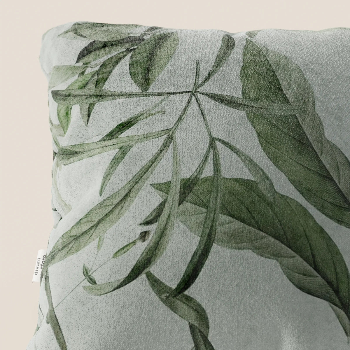 The Lemon elegante cuscino a fantasia in velluto impermeabile verde di divitt.sbs presenta un motivo botanico di foglie verdi sovrapposte su sfondo grigio chiaro, con etichetta bianca sul lato e fondo beige.