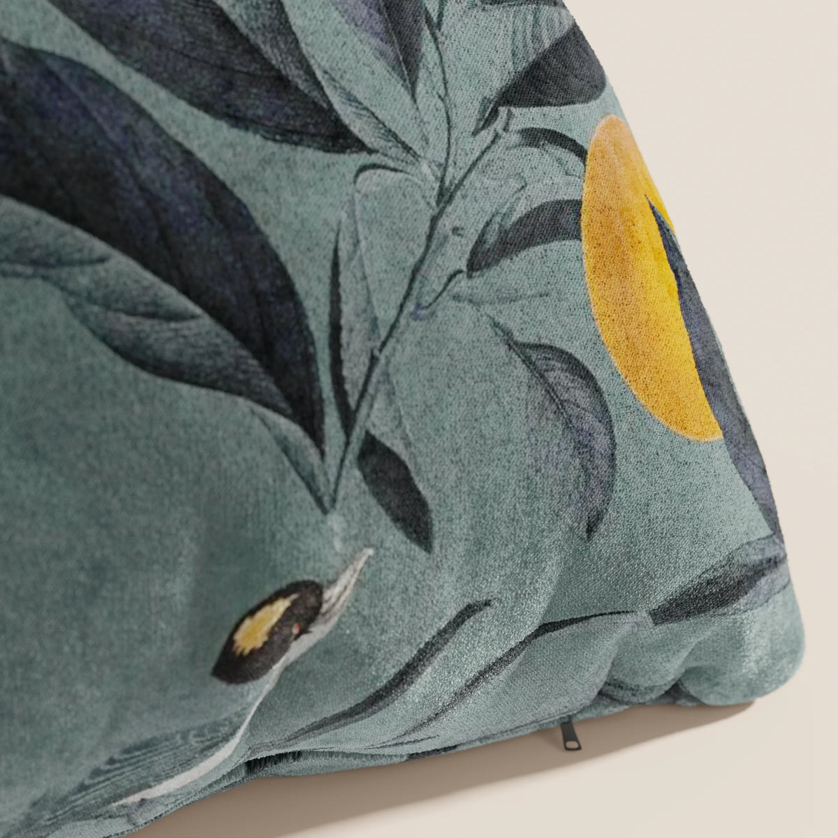 Un primo piano del cuscino Lemon elegante a fantasia in velluto impermeabile petrolio di divitt.sbs, che mostra stampe botaniche blu scuro, un cerchio giallo e parte di un uccello, uno dei nostri cuscini decorativi lavabili.