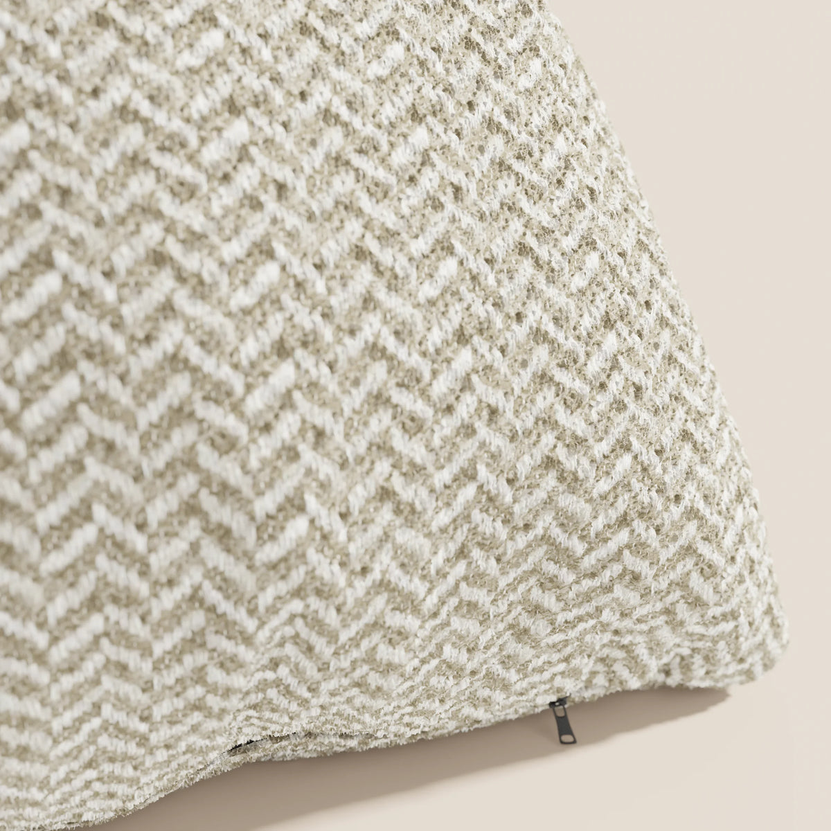 Un primo piano del modello "Sorrento Cuscino 45x45 in Lino" di divitt.sbs mette in risalto la sua trama a spina di pesce nei toni del beige e del bianco, i delicati dettagli intrecciati e un piccolo tirazip nero su uno sfondo beige chiaro a tinta unita.