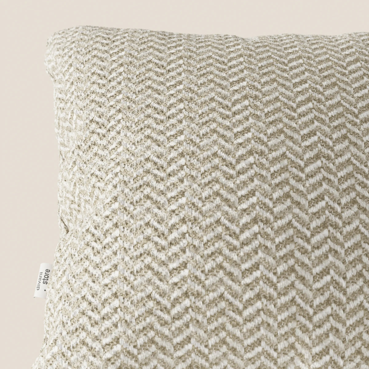 Un primo piano del cuscino Sorrento 45x45 in Lino di divitt.sbs ne mette in risalto la trama a chevron nei toni del beige e del bianco, il tessuto testurizzato e la piccola etichetta laterale. Questo elegante cuscino, lavabile in lavatrice, spicca su uno sfondo bianco sporco.