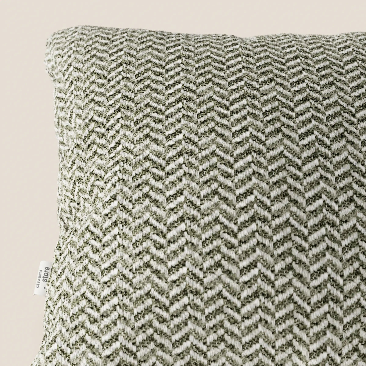 Primo piano del cuscino Sorrento 45x45 in lino di divitt.sbs, che ne mette in risalto la trama a spina di pesce nei toni del verde oliva e del crema. Questo cuscino, lavabile in lavatrice, presenta una piccola etichetta laterale bianca su uno sfondo beige chiaro a tinta unita.