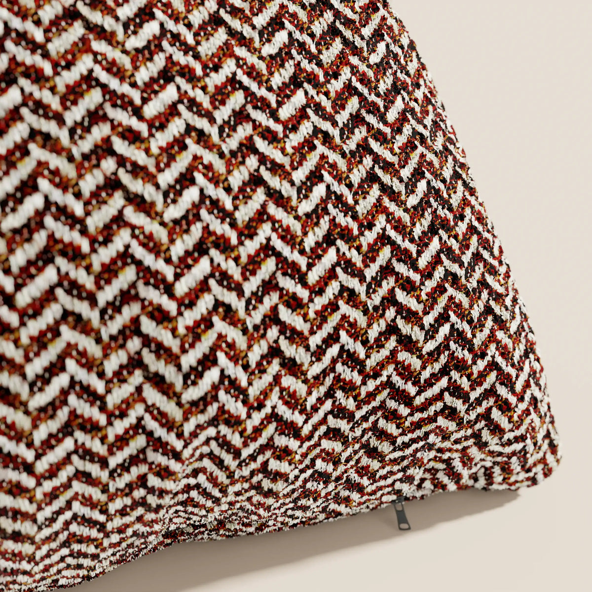 Primo piano del cuscino Sorrento 45x45 in lino di divitt.sbs, che mette in risalto il suo morbido tessuto con motivo a chevron nei colori rosso, marrone, nero e bianco: un elegante esempio di cuscini lavabili in lavatrice su uno sfondo beige.